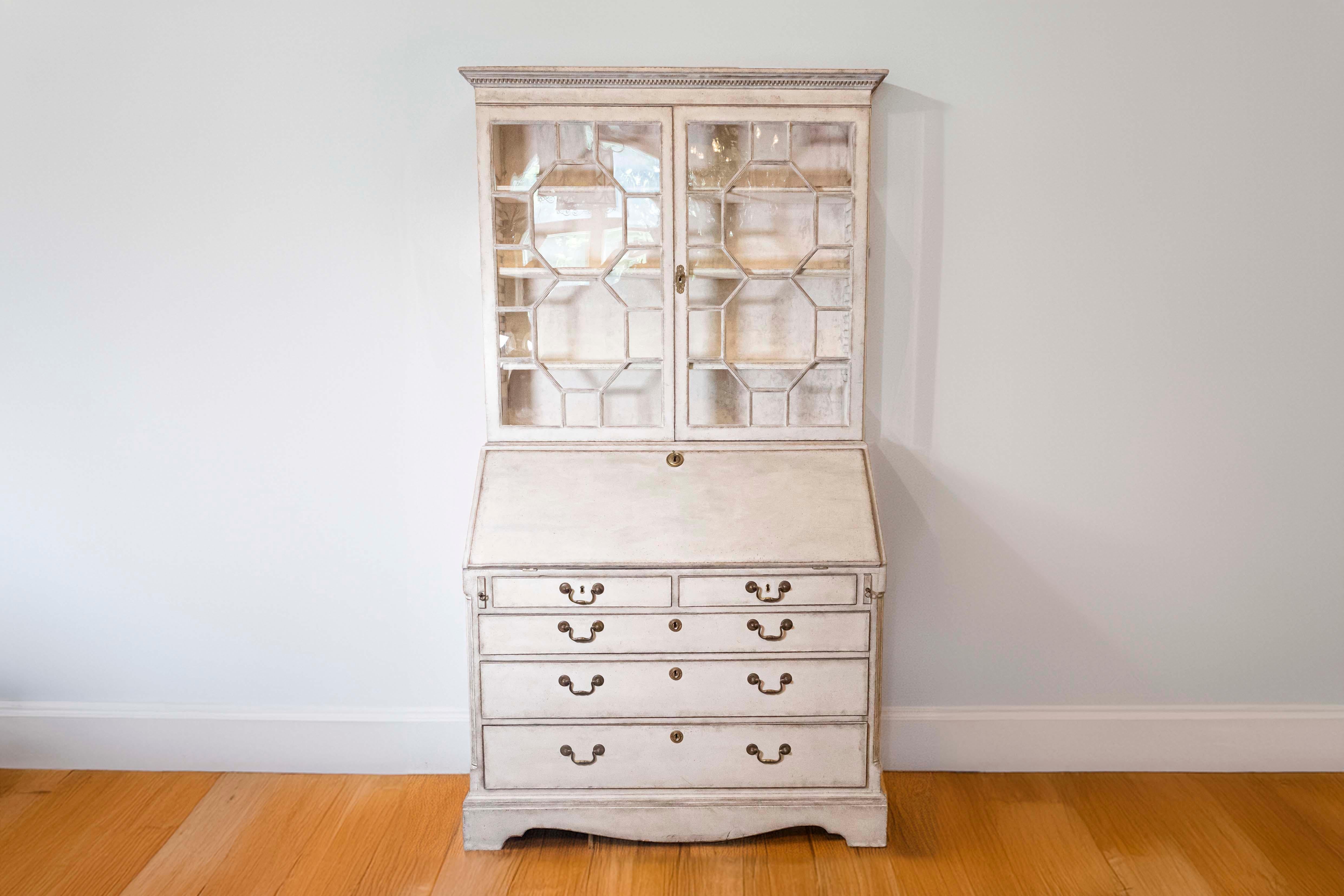 A European two-part tall secretary from the 18th century with gray / cream painted finish, old glass doors, slant front desk and five graduated drawers. Discover elegance and functionality intertwined in this stunning 18th-century European two-part