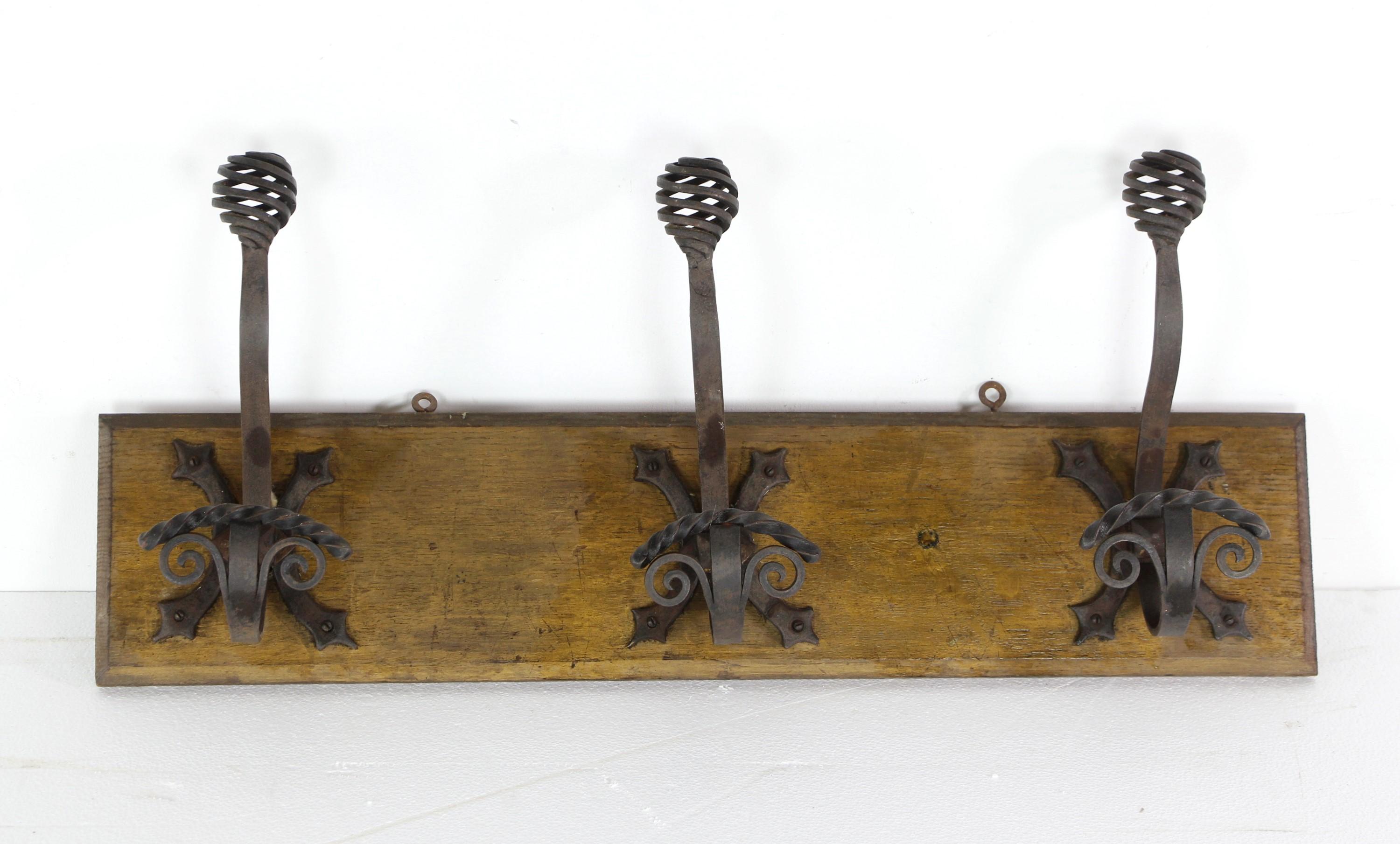 European wall rack featuring three curled wrought iron hooks mounted on a wood base. This piece combines traditional wrought iron craftsmanship with a touch of European charm, providing a functional and decorative solution for hanging items in