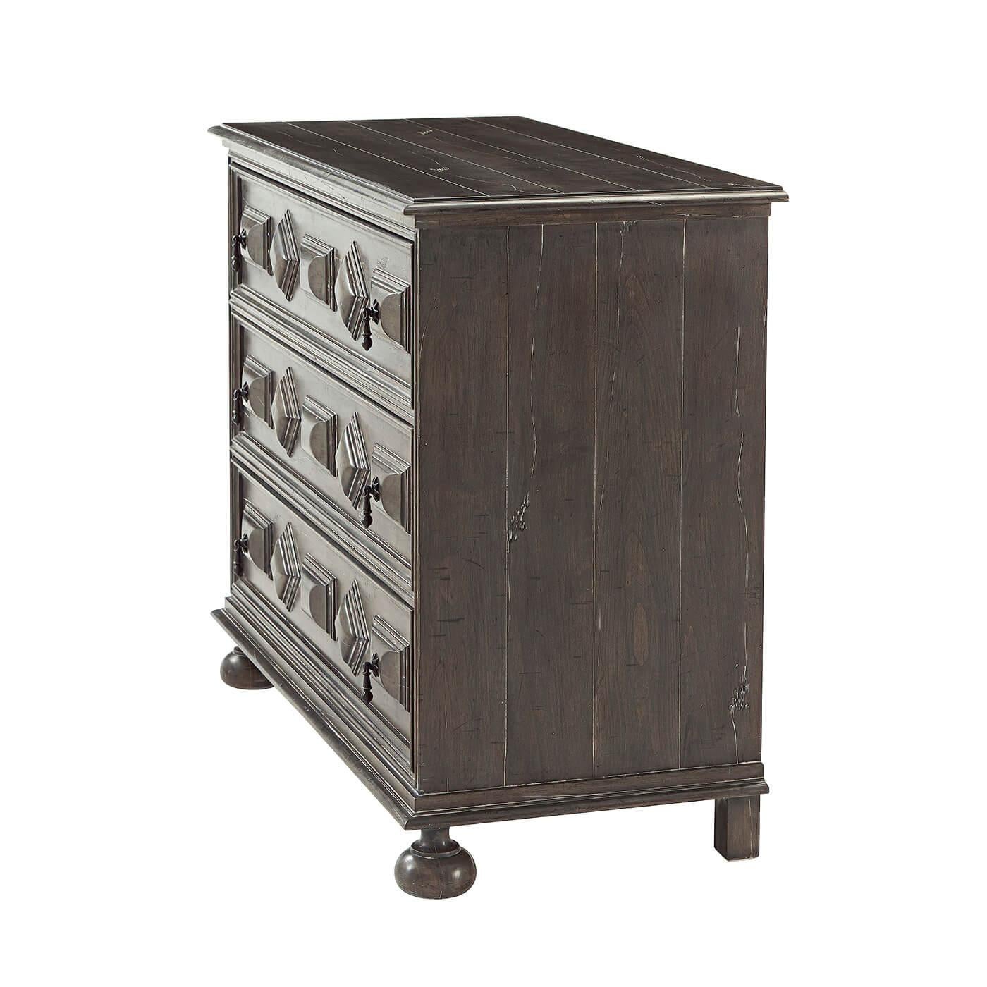 An early European style three drawer antiqued chest of drawers, with a planked molded edge top, three deep relief paneled drawers with brass drop handles and bunn feet.

Dimensions: 42