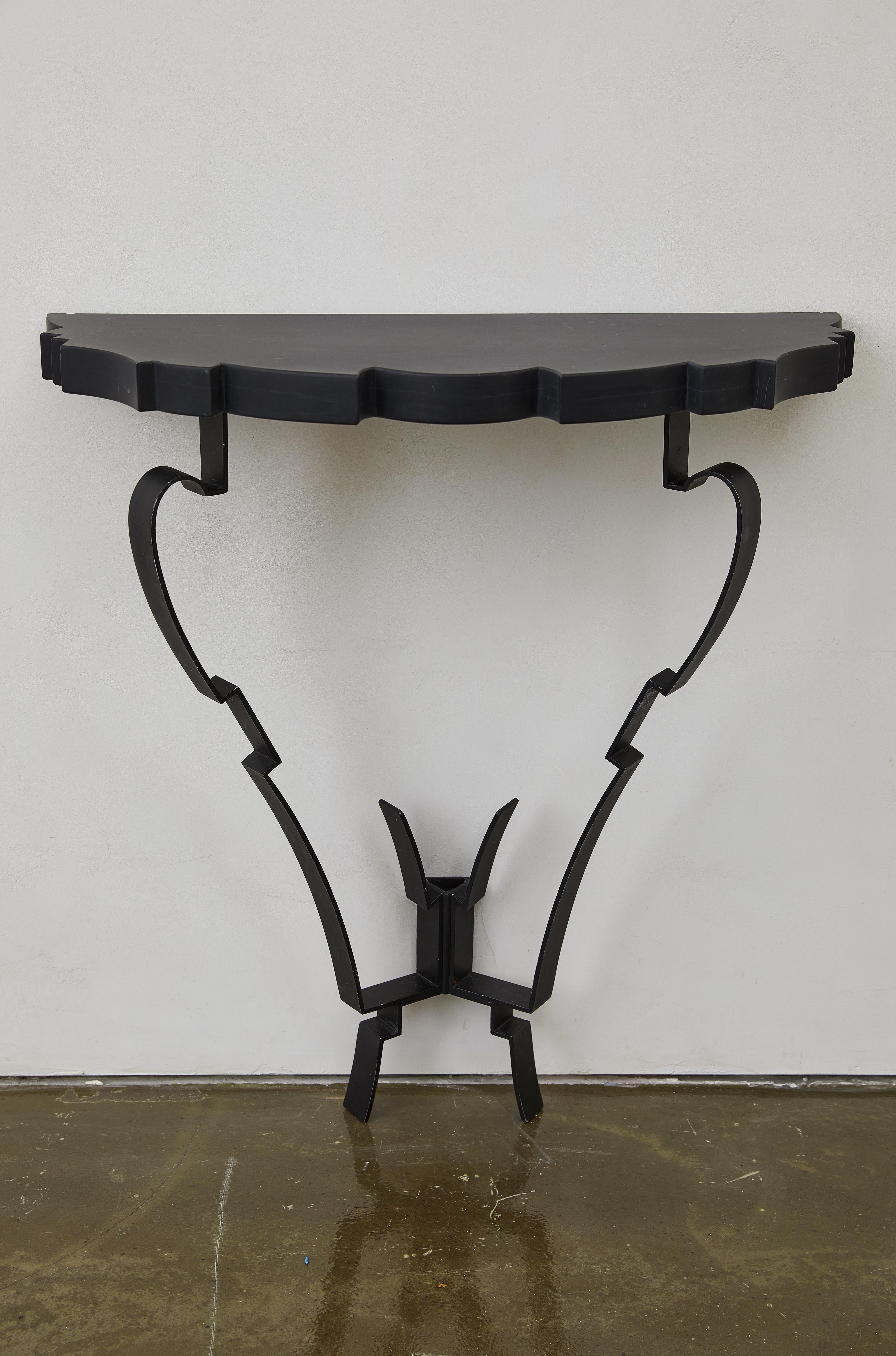 This Art Deco-inspired European console table features a striking scalloped granite top, supported by an elegant yet angular black iron base. The sculptural wall-mounted frame showcases a dynamic interplay of curved and geometric elements,