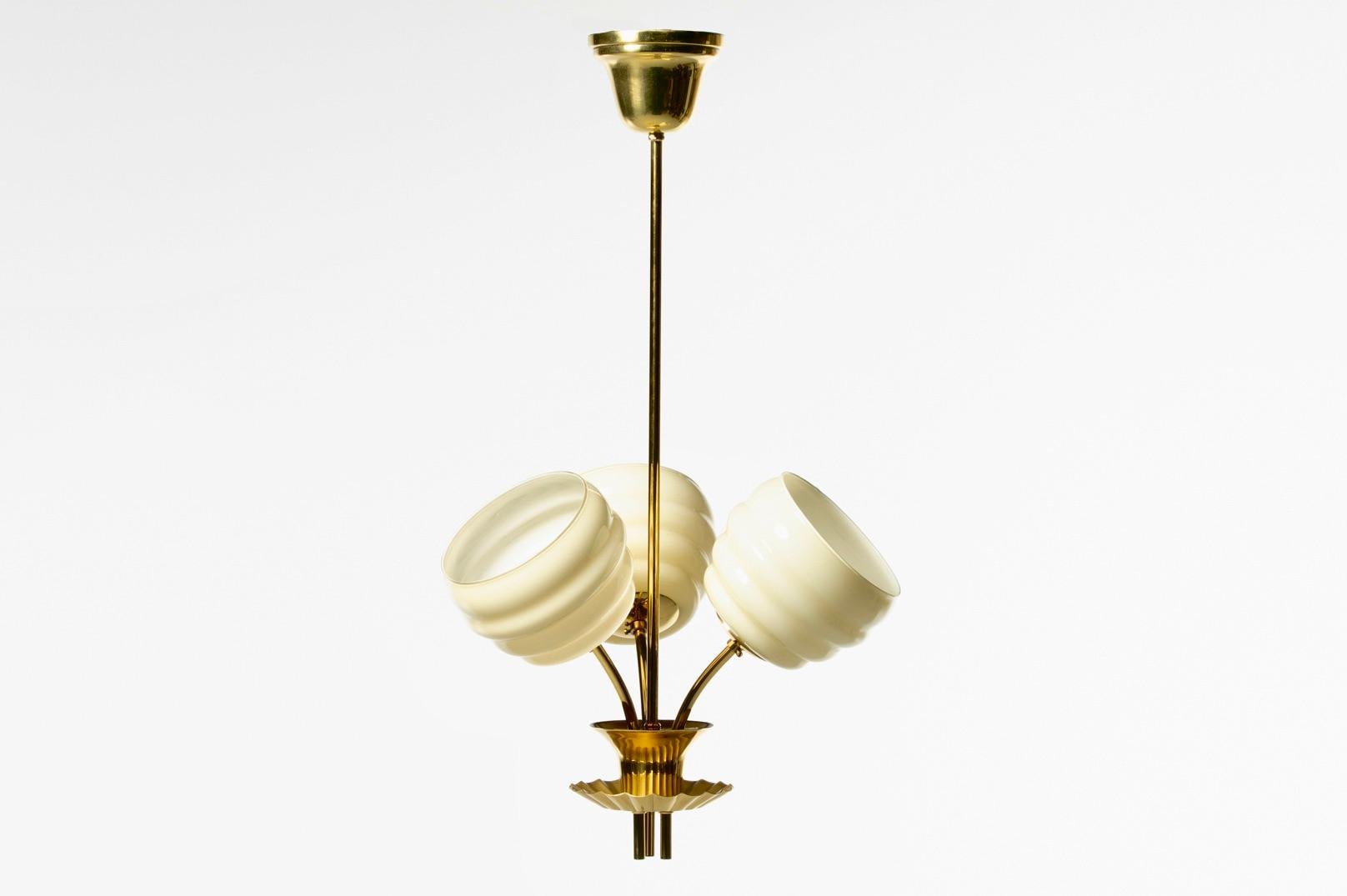 Hailing from Denmark and dating back to the 1930s is this glamorous Paavo Tynell style Art Deco brass and glass three light pendant. Beautiful and unique, the pendant features three channeled glass diffusers reminiscent of small bee hives. The