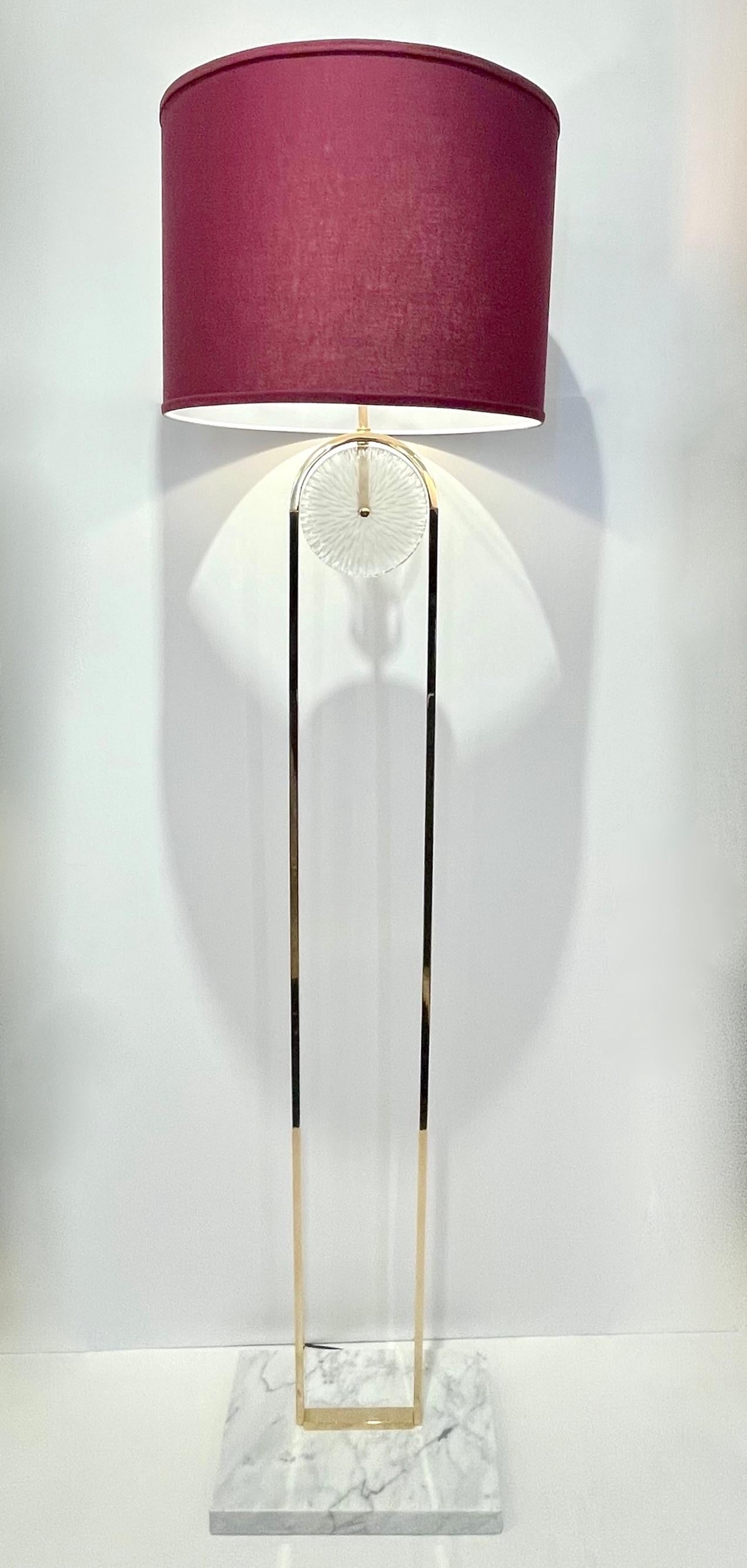 A pair is available now - A minimalist floor lamp, entirely handcrafted in Spain, with Art Deco flair and Hollywood regency glamour,  consisting of a hand-made curved brass structure decorated with a textured Murano glass disc, raised on a Carrara