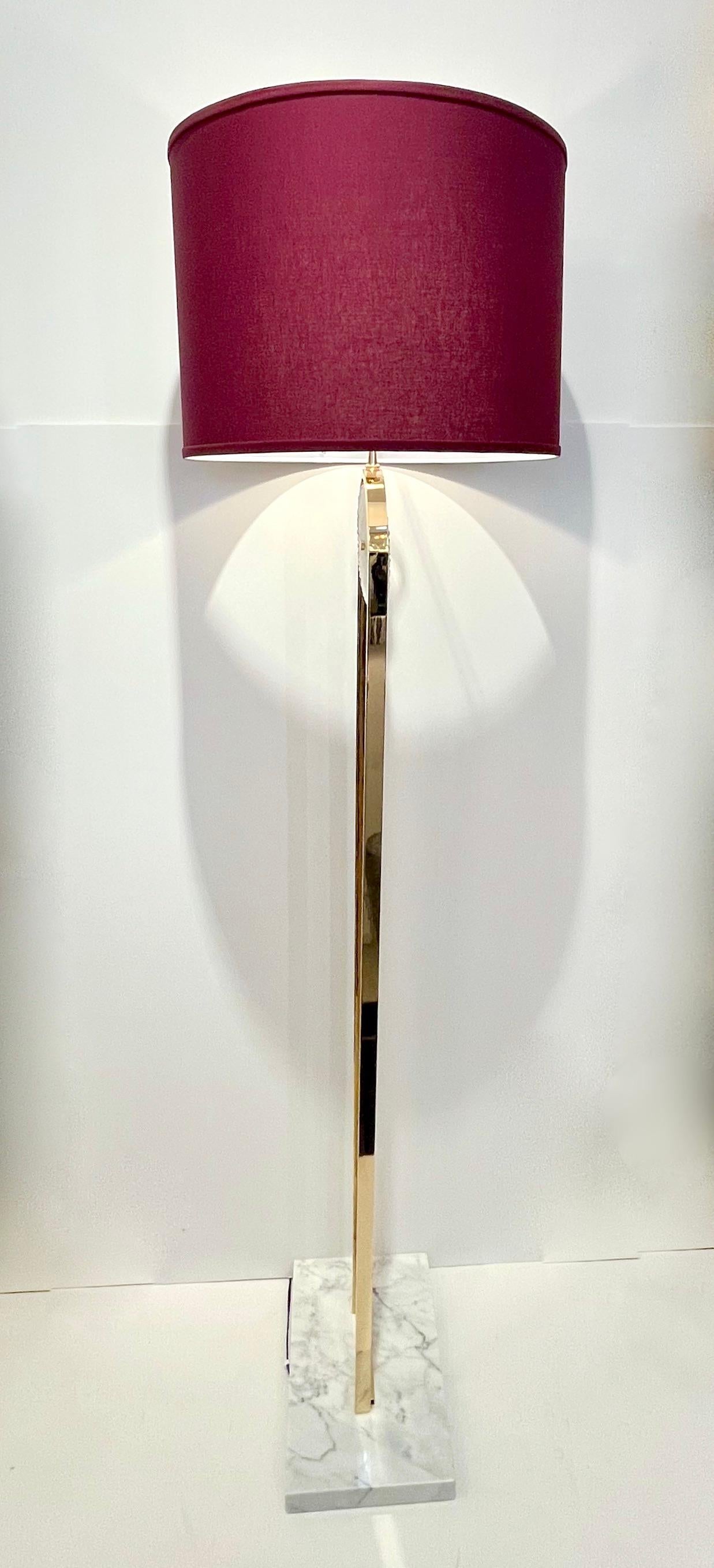A pair is available now - A minimalist floor lamp, entirely handcrafted in Spain, with Art Deco flair and Hollywood regency glamour,  consisting of a hand-made curved brass structure decorated with a textured Murano glass disc, raised on a Carrara