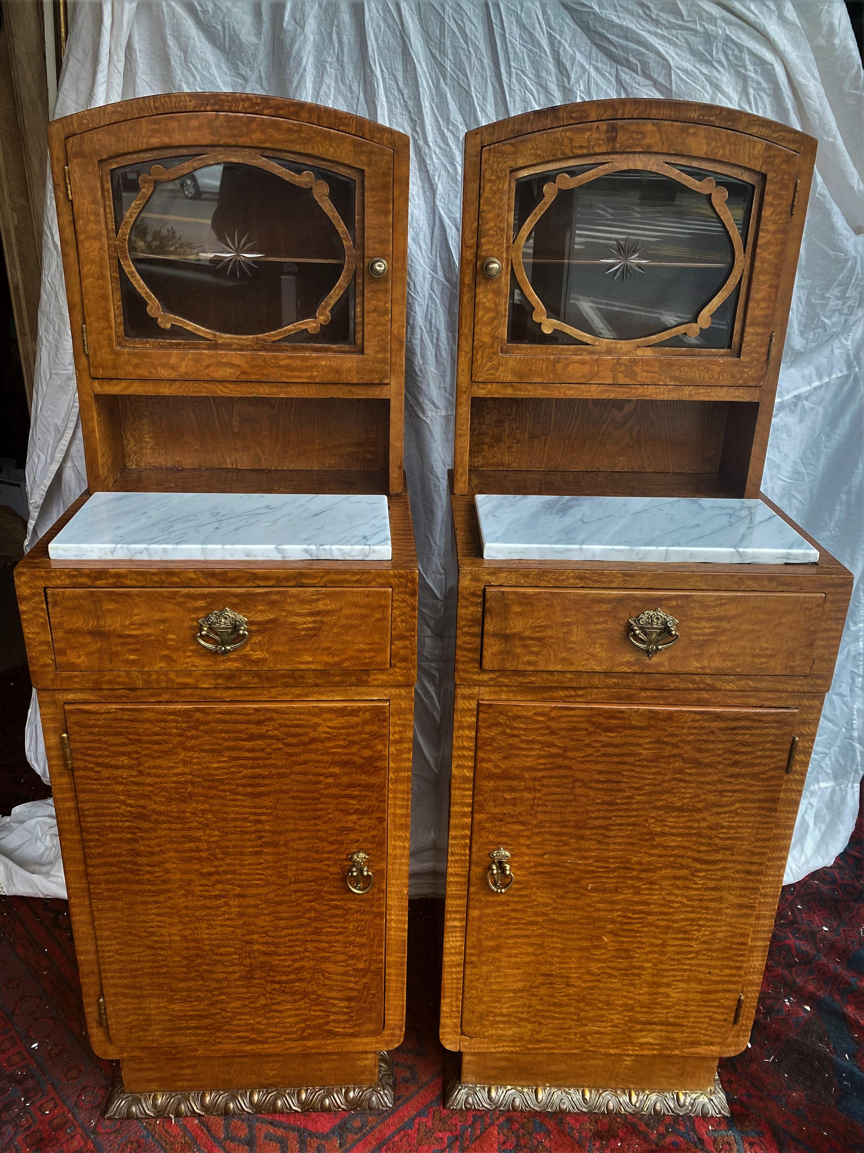 These are the sweetest pair of side tables with a lovely burled wood finish and brass tone cast metal hardware with floral decoration. The top section has glass front doors with etched stars at centers and wood overlay decoration which opens to