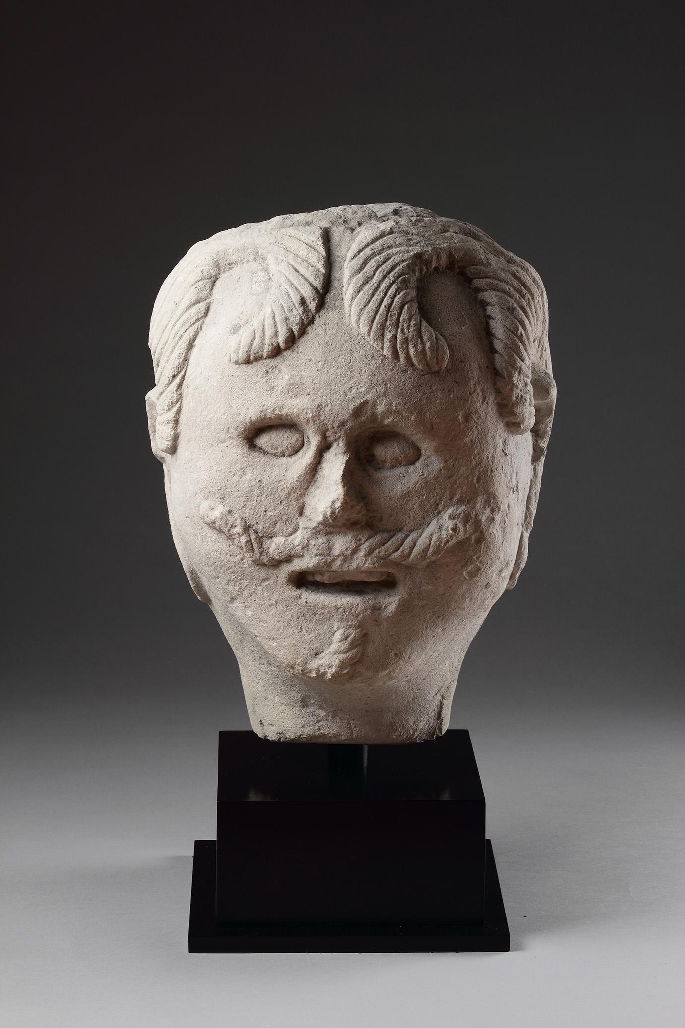 A Large European Carved Limestone Celtic Votive Head of a Male Warrior Wearing a Typical Flowing Moustache Small Beard and Curling Locks of Hair Stiffened with Lime Wash the Slit Mouth Open as if in Command
Circa 1st Century BC - 1st Century