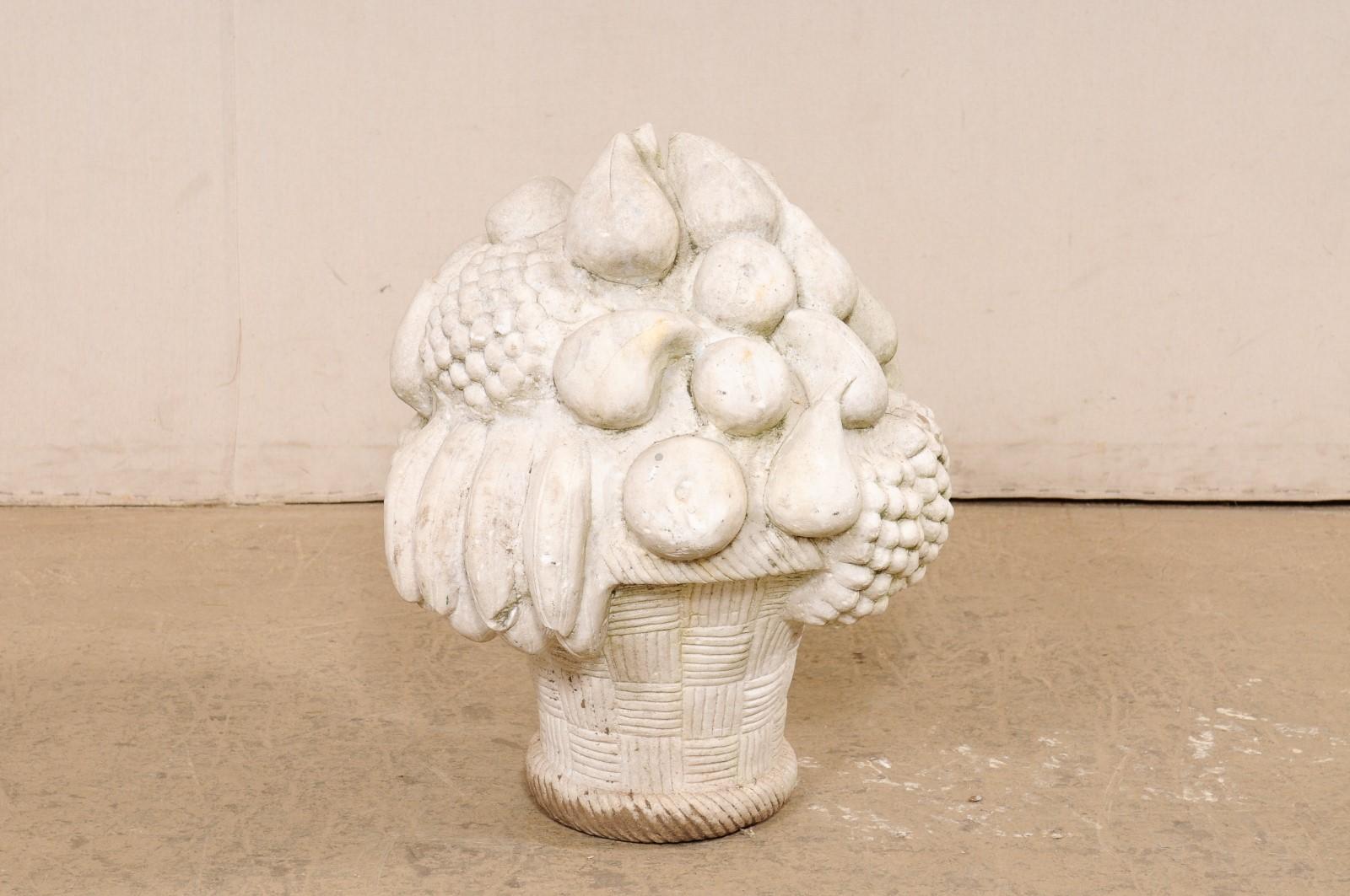 A European carved-stone basket of fruit garden statue. This vintage ornament from Europe has been hand-carved of stone (likely marble) in the image of a hand-woven basket overflowing with a fruit bouquet of grapes, pears, bananas, and apples. The