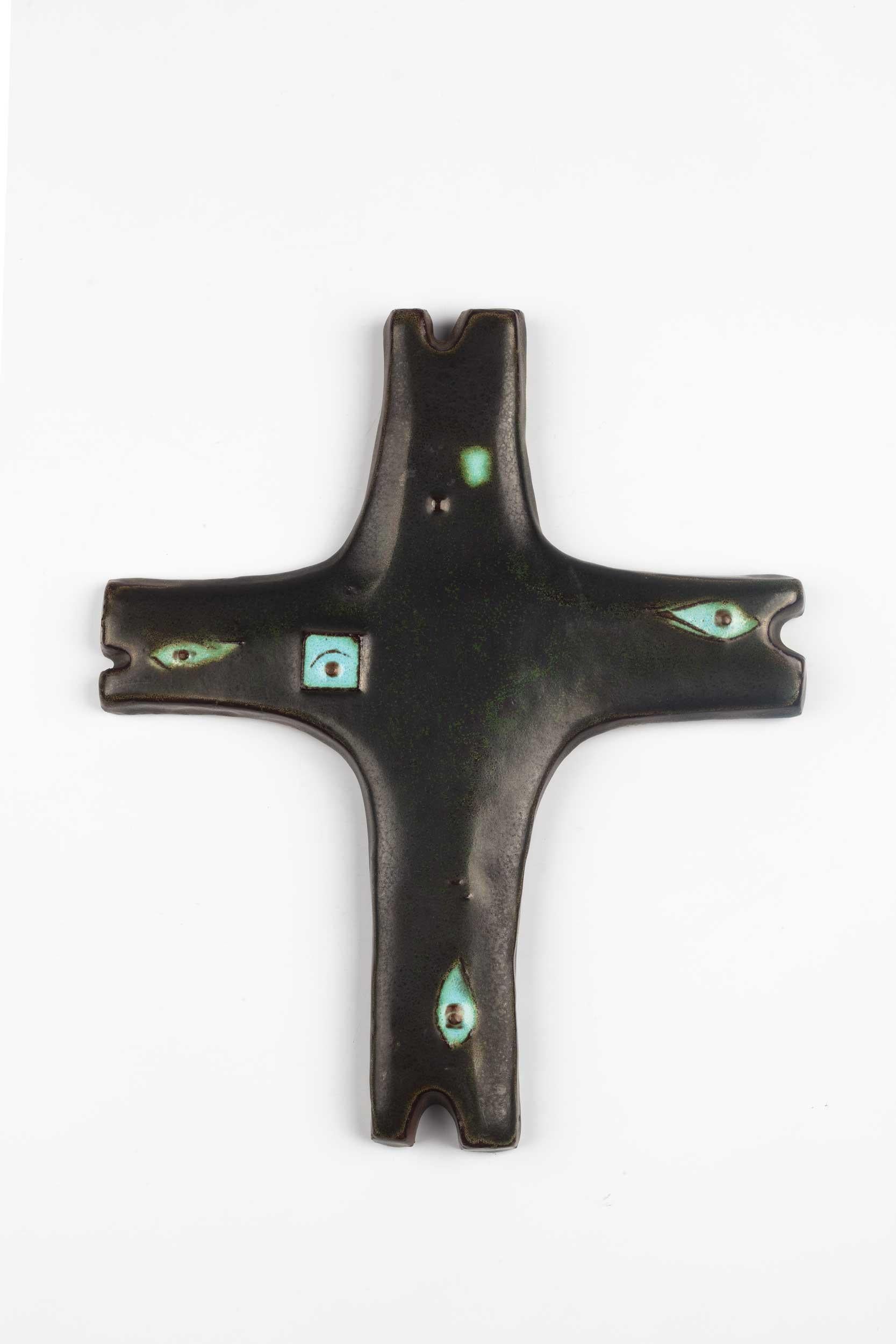 Belgian wall cross in ceramic, hand painted in semi-gloss earthy black with decorative turquoise colored eye shapes throughout. 

From modernism to brutalism, the crosses in our collection range from being as futurist as a modernist church to as