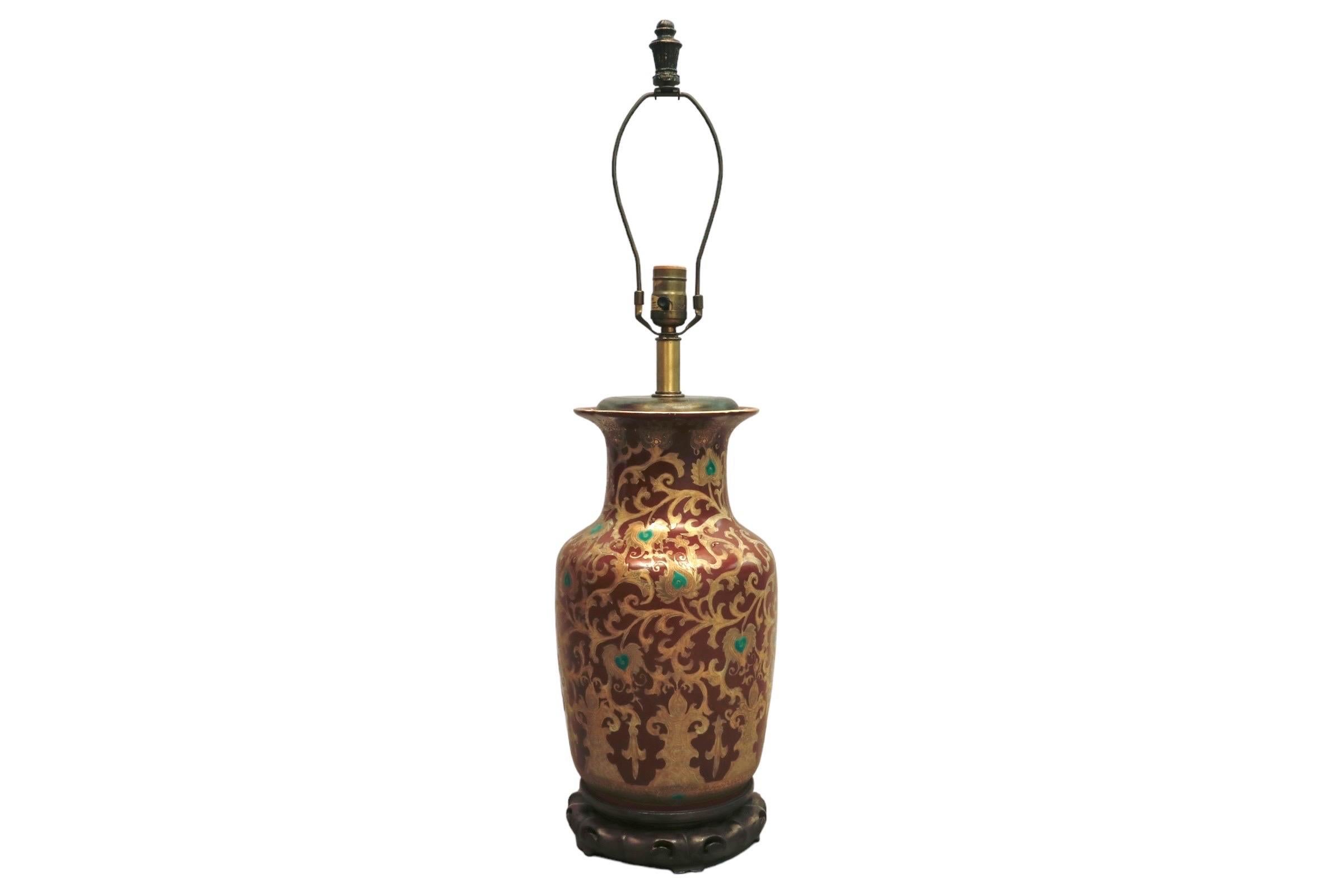 A European Chinoiserie ceramic table lamp. Decorated with an exotic gilt vine motif, hand painted with jade green hearts at the center of vine leaves and red throughout the body. The wooden base is carved and pierced, and brushed with a gold finish