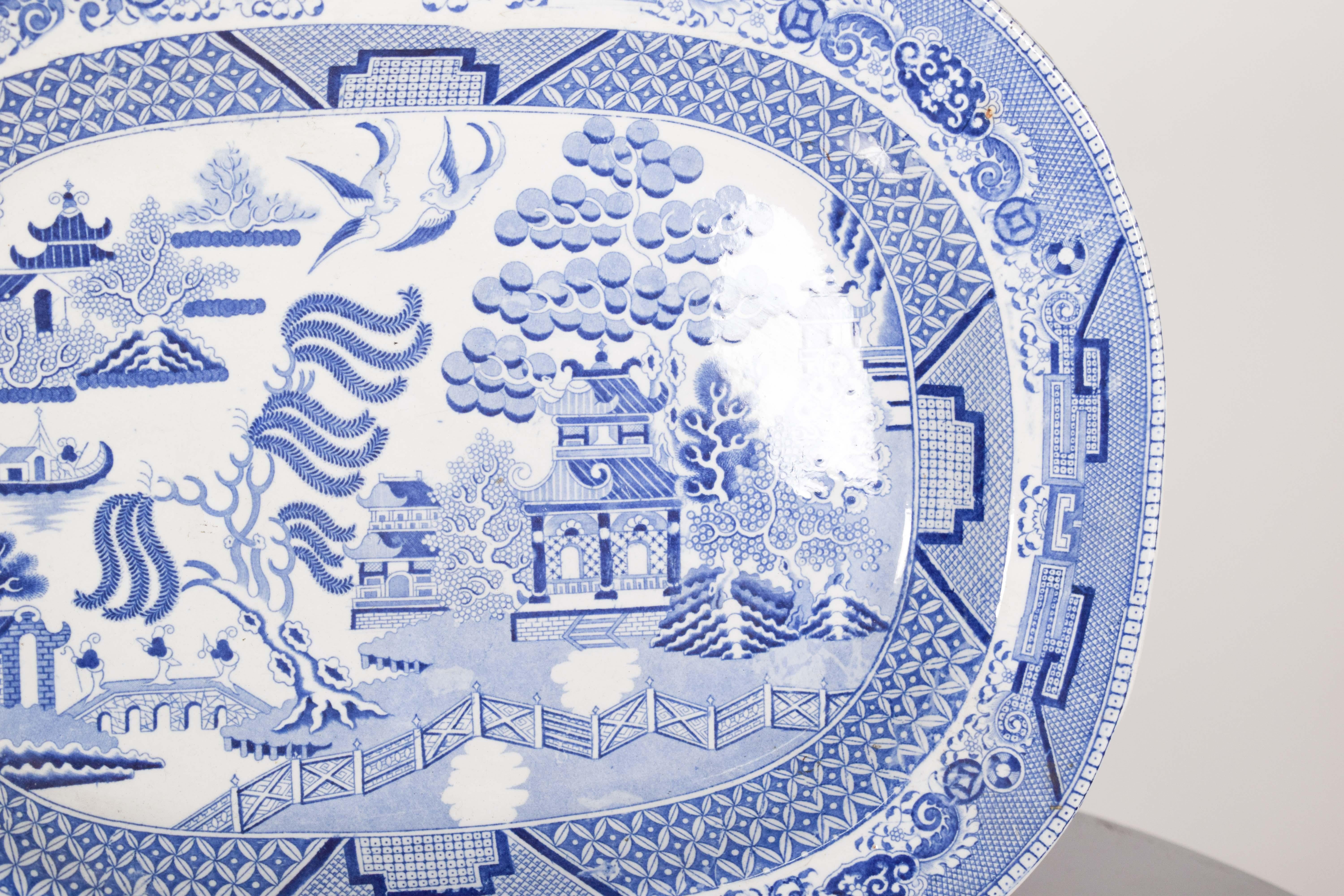 Teller aus europäischem Steingut, mit asiatischem Dekor. In der Mitte befindet sich eine kunstvolle Landschaft mit einer bogenförmigen Brücke, auf der kleine Figuren spazieren gehen. Daneben steht eine Pagode in traditioneller chinesischer