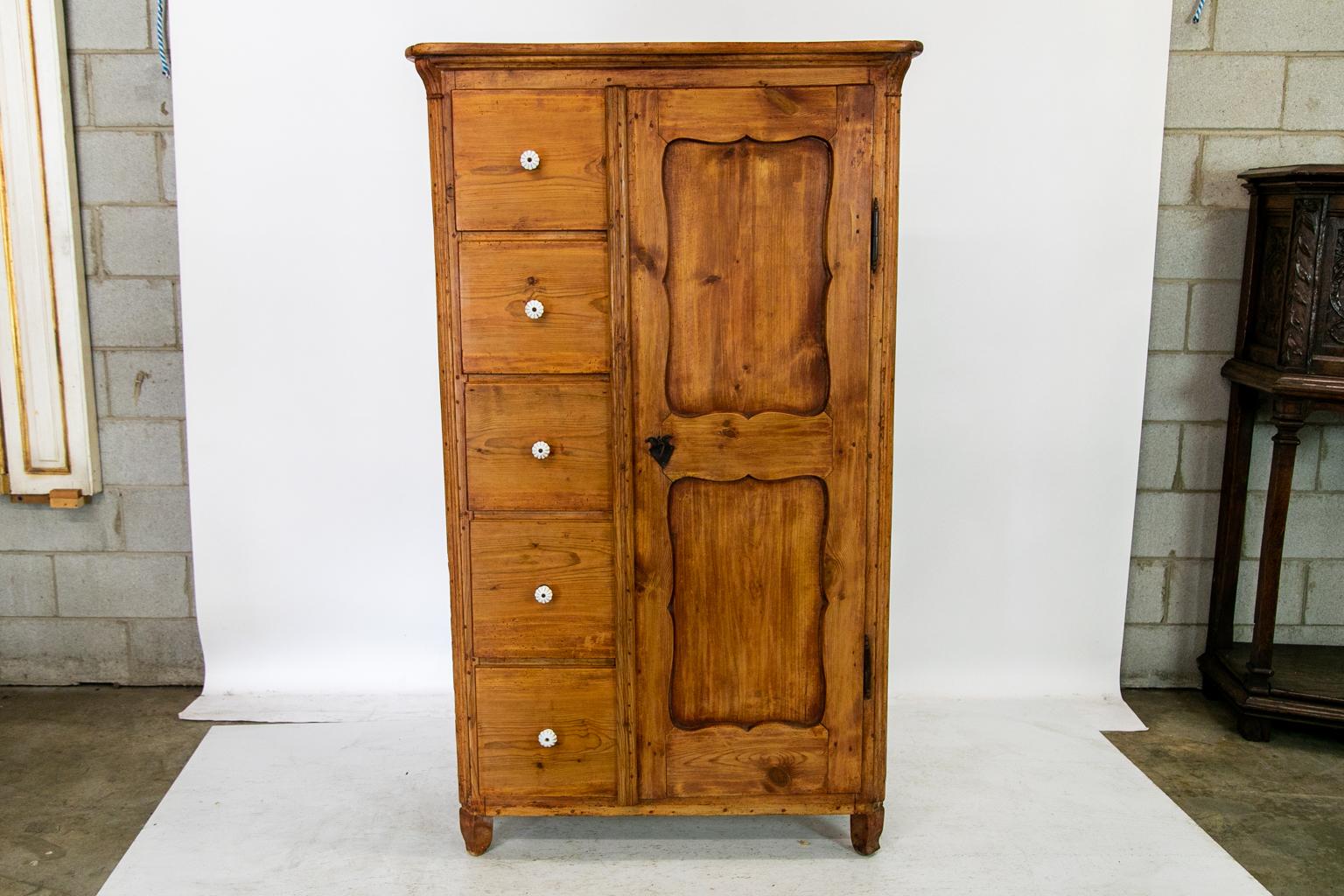 Cette armoire en pin a deux panneaux en retrait dans la porte qui a une construction apparente à double chevilles avec la serrure originale en acier et l'écusson en trou de serrure. Les cinq tiroirs ont des boutons champignons en porcelaine