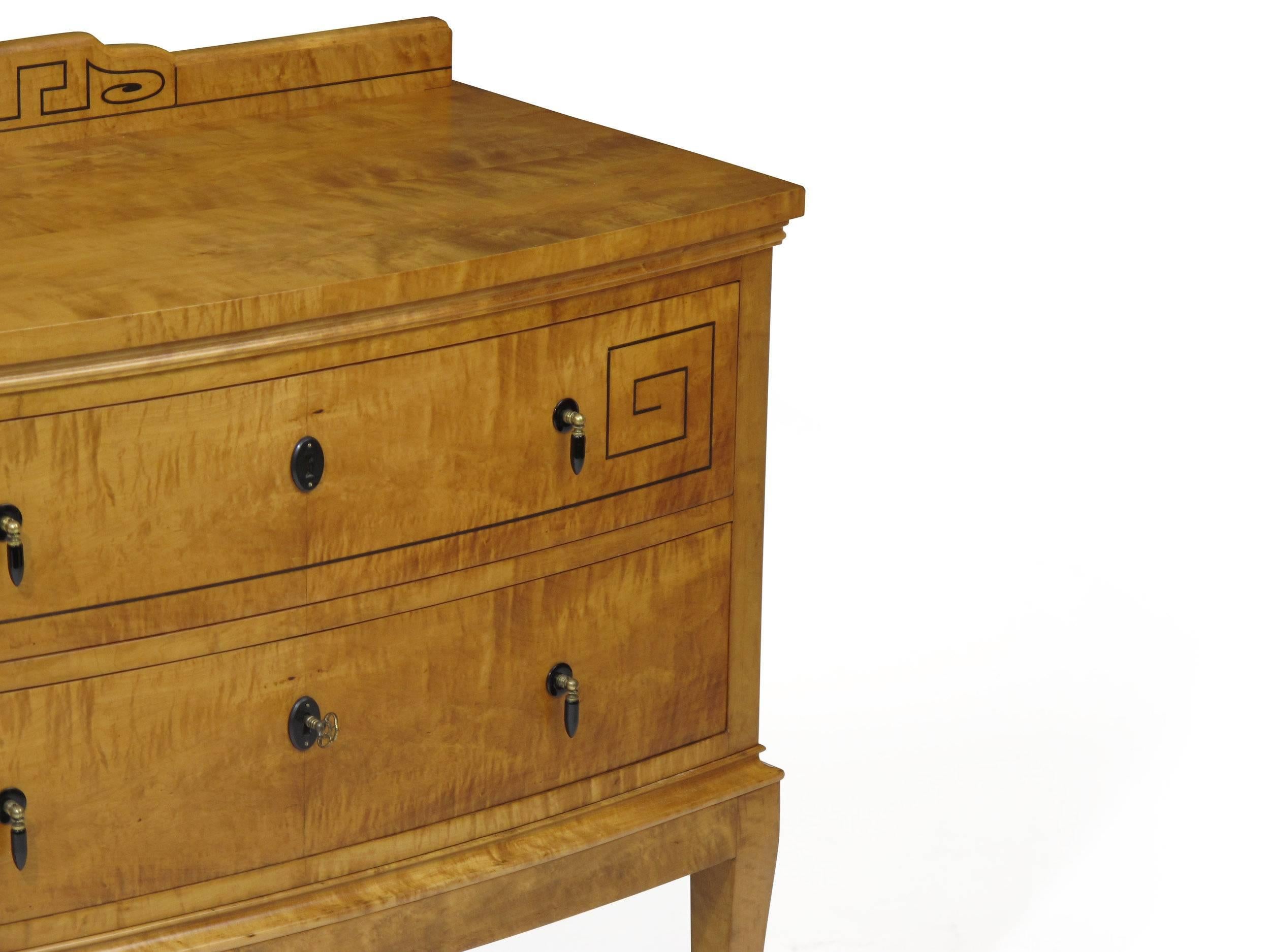 Exquisitely grained flamed birch chest of two drawers with inlay flourishes of ebony and tear-drop pulls.  Splayed saber legs giving it sturdy support. Drawers with dovetail joinery are curved outwards adding a gentle dynamic to the console while a