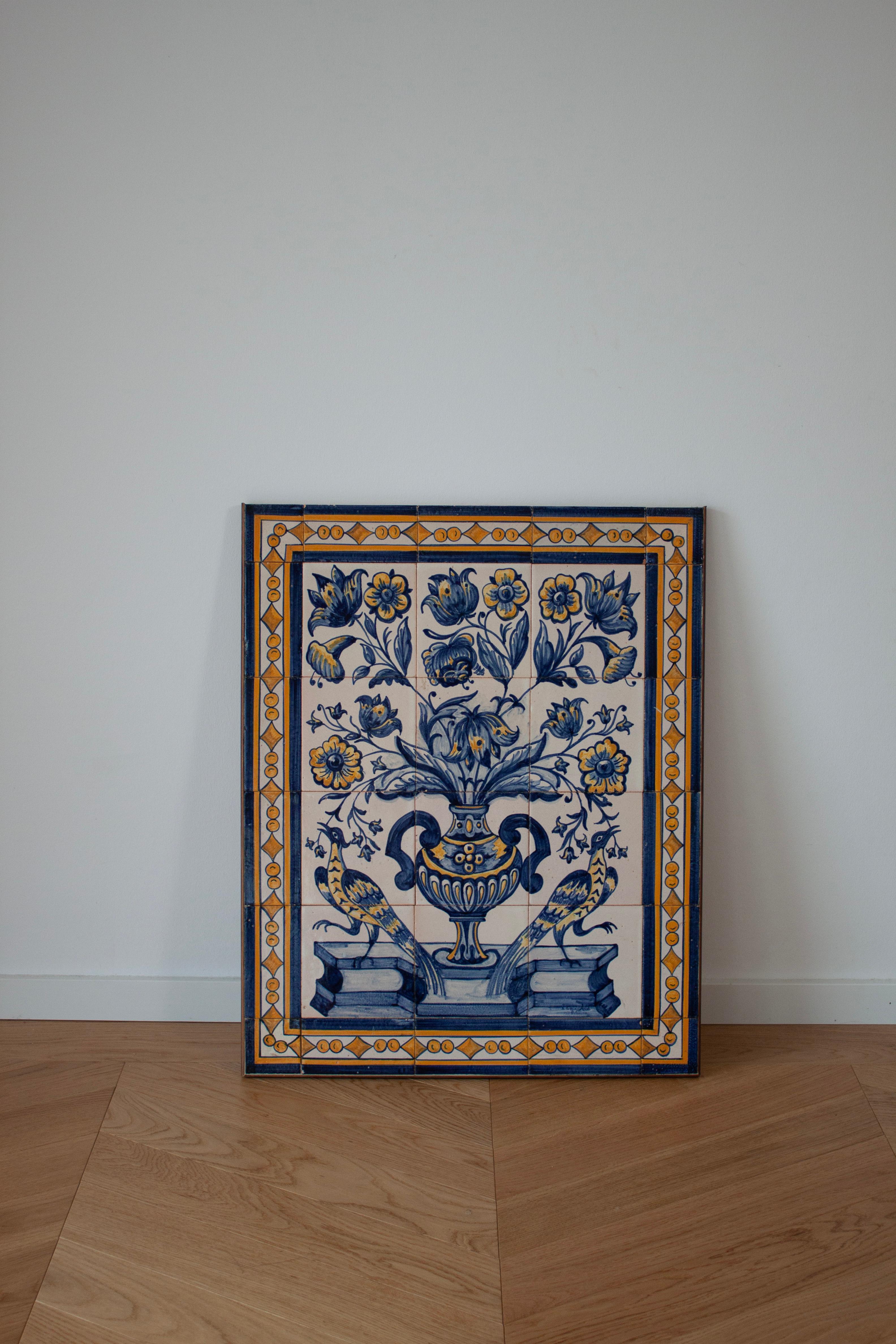 On offer is a beautiful piece of tiled artwork, showcasing intricate floral and animal motifs, painted in a blend of blue, white, and yellow tones. Each tile is hand-painted, depicting a scene of two peacocks, an elegant vessel, and blossoming