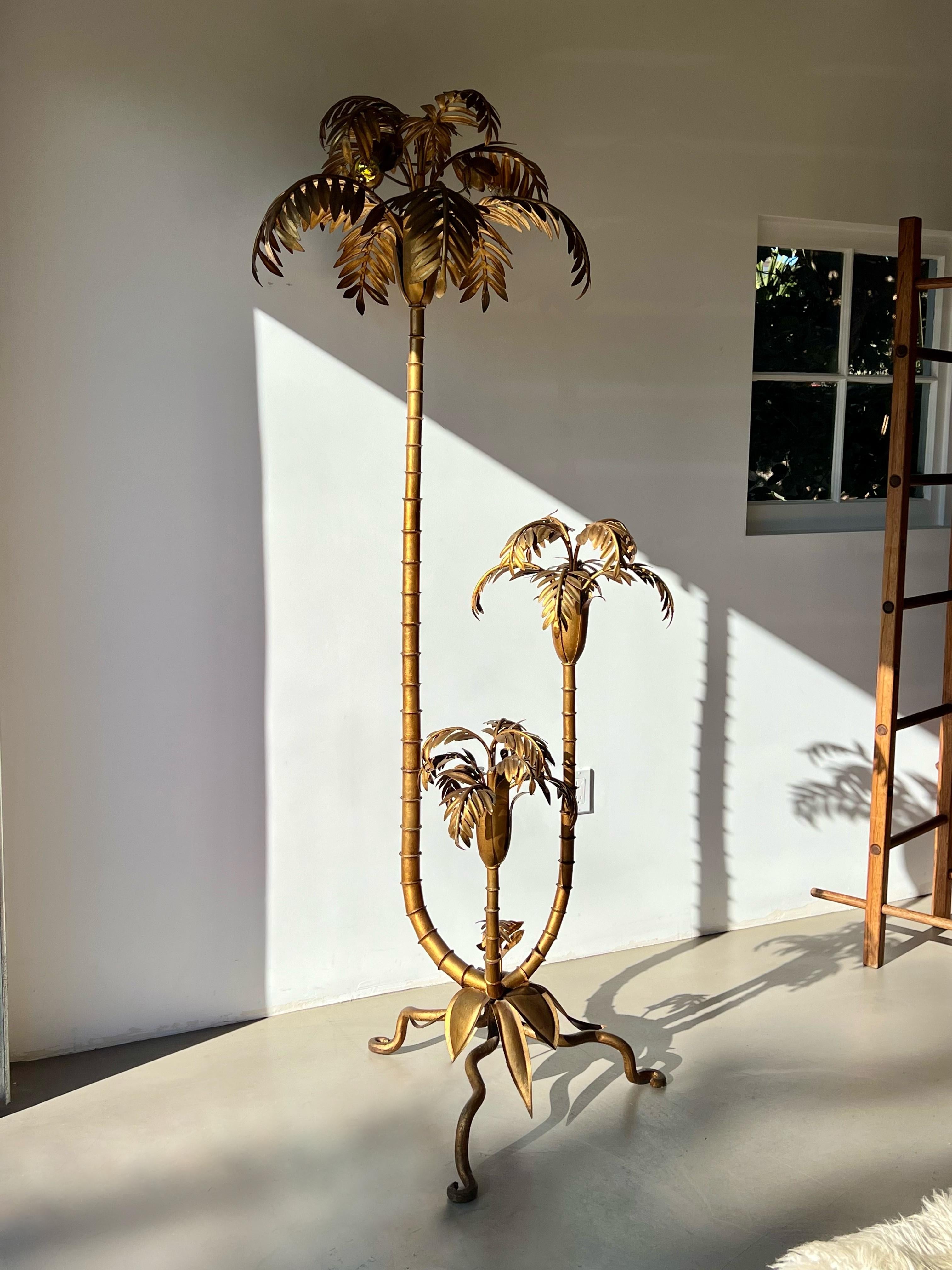 Una straordinaria lampada da terra a forma di palma dorata in stile Hollywood Regency, attribuita a Hans Kögl, degli anni '60-'70 circa. Questo pezzo scultoreo è caratterizzato da tre tronchi di palma elegantemente curvati, ciascuno ornato da fronde