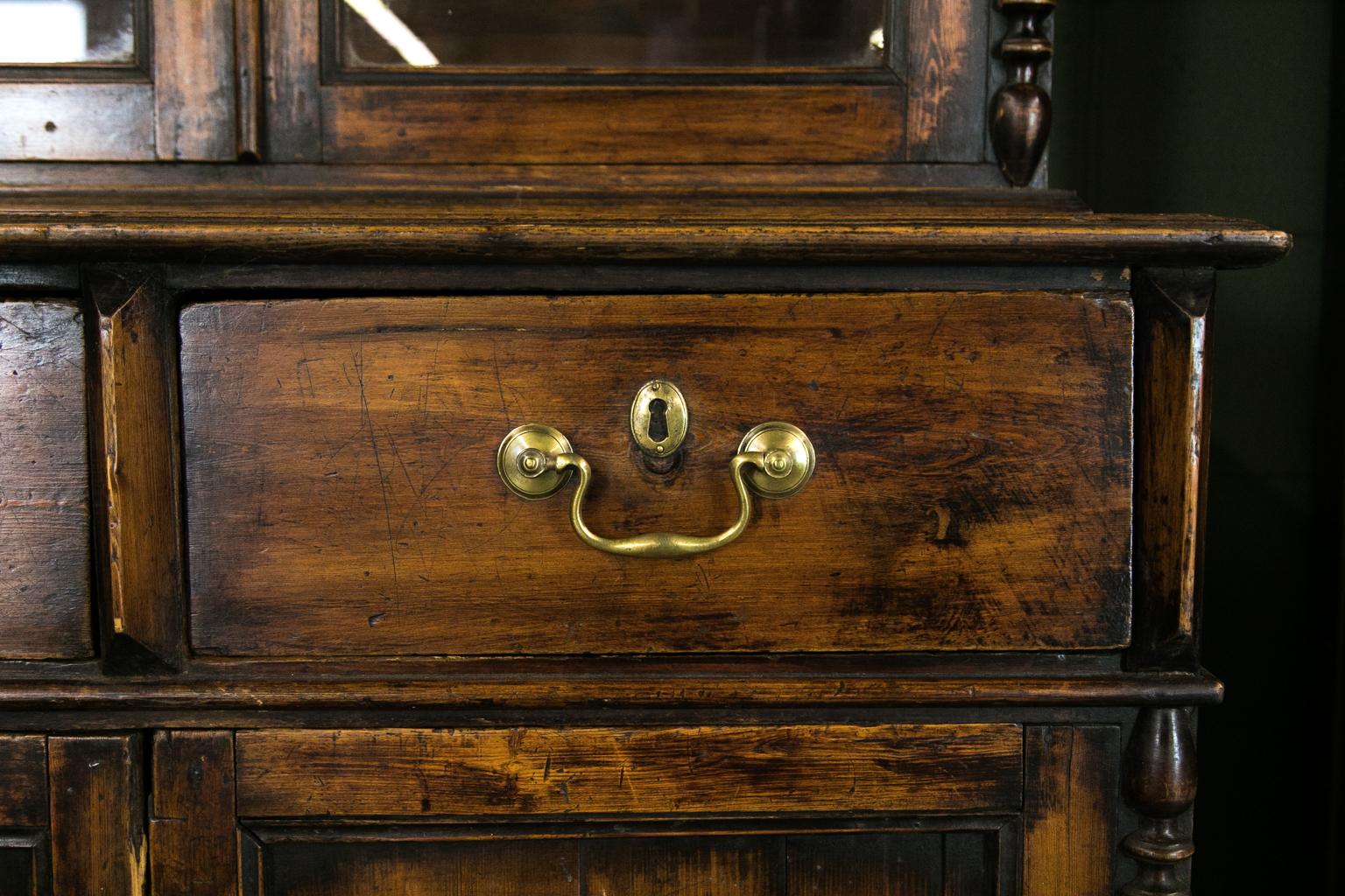 European glass door cupboard has traces of the original red paint, the top featuring a broken arch pediment and finial. There are turned applied spindles to the stiles. Six wavy glass panes are framed with carved moldings.
 