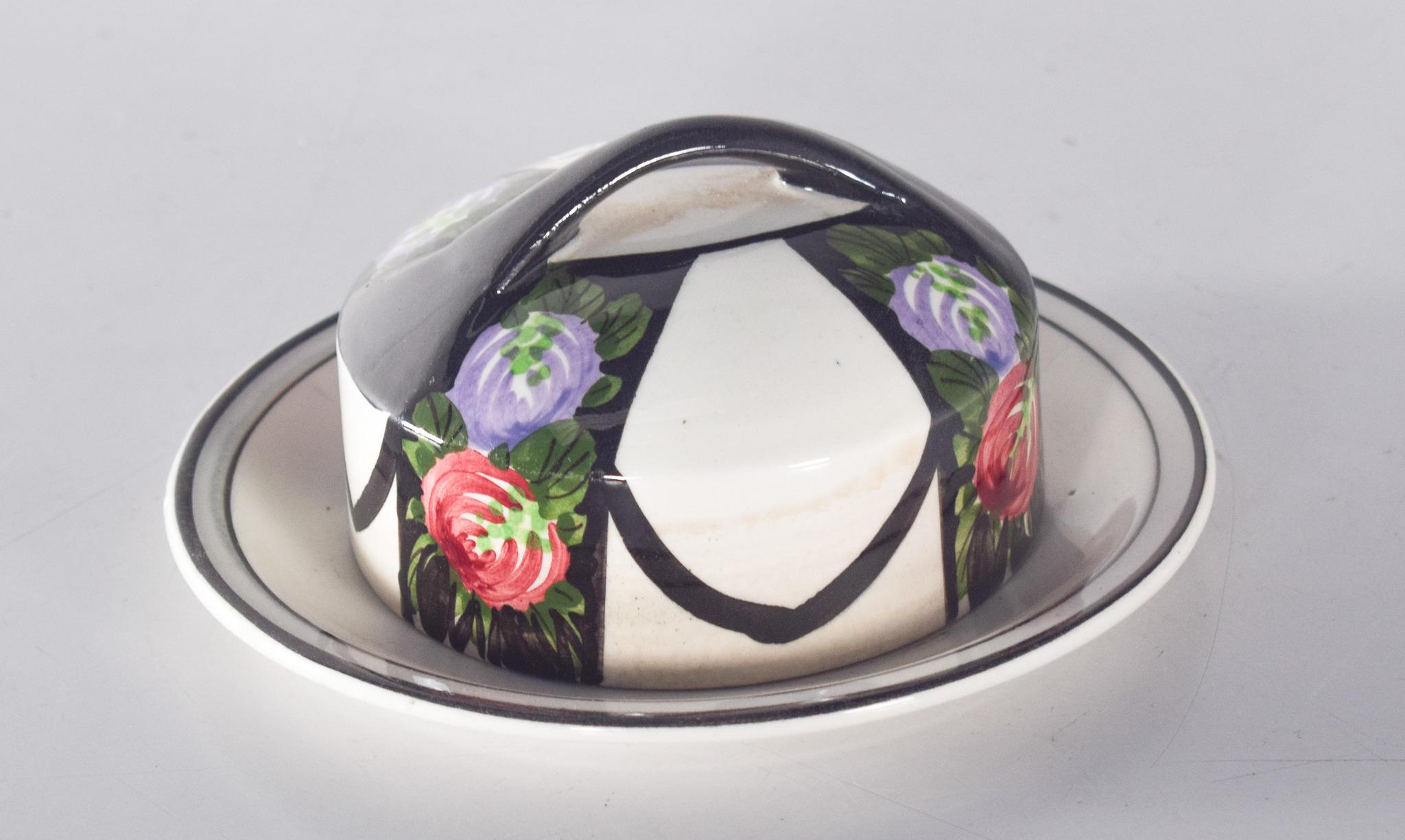 Mantequera de cerámica esmaltada. Con decoración policromada de flores pintadas a mano, incluye rosas rojas y lilas enmarcadas por exuberantes hojas verdes, creando un aspecto delicado y romántico. La tapa, con un asa integrada en la parte superior