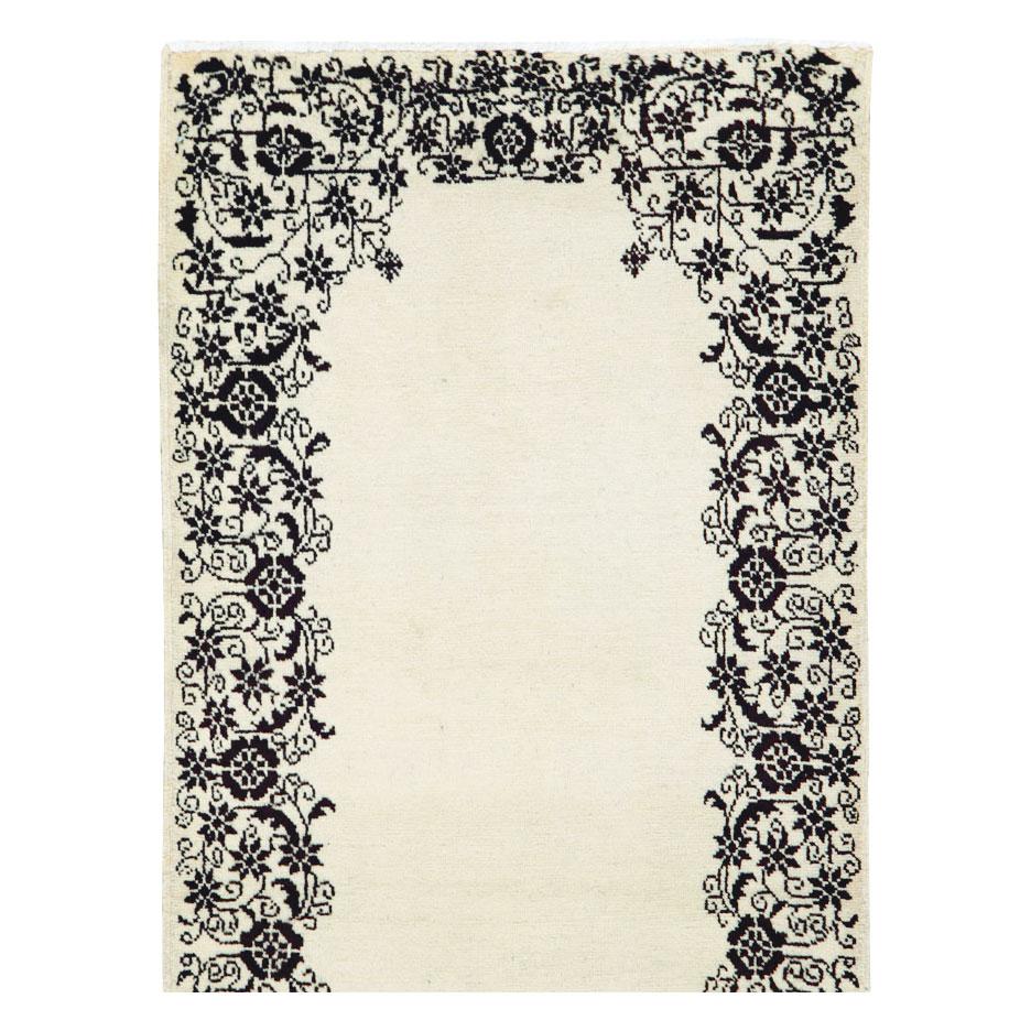 A vintage Persian Tabriz rug in runner format handmade during the mid-20th century with a plain solid white field and a black border inspired by European floral design. Complete flowers, rosettes, and tight vinery make up the intricate