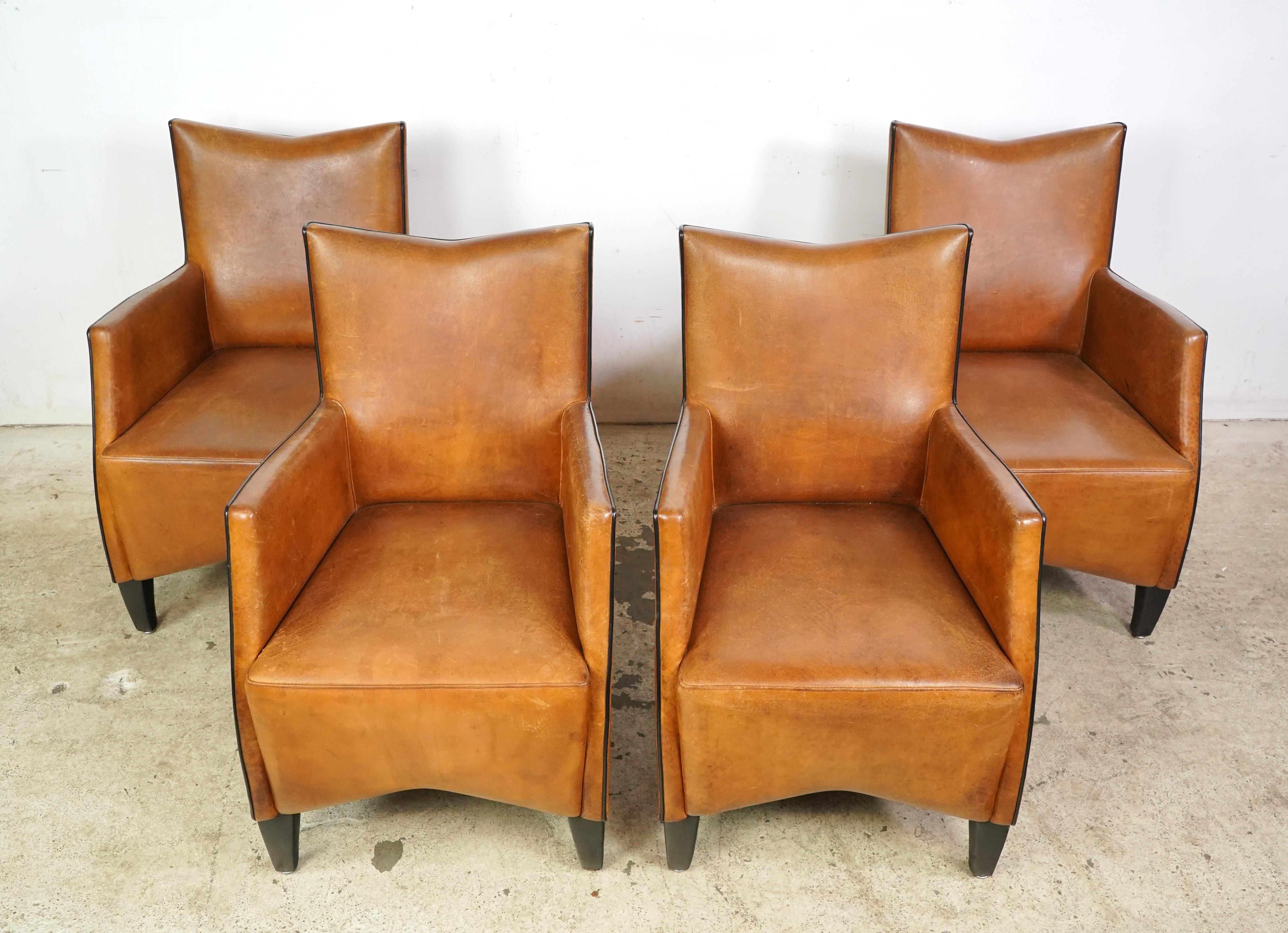 Mid-Century Modern leather dining chairs made in France. The chairs have a distinct shape with a slightly angled back and a seat that appears to be wide, and black painted wooden legs. The leather and feet show signs of wear and age. Please refer to