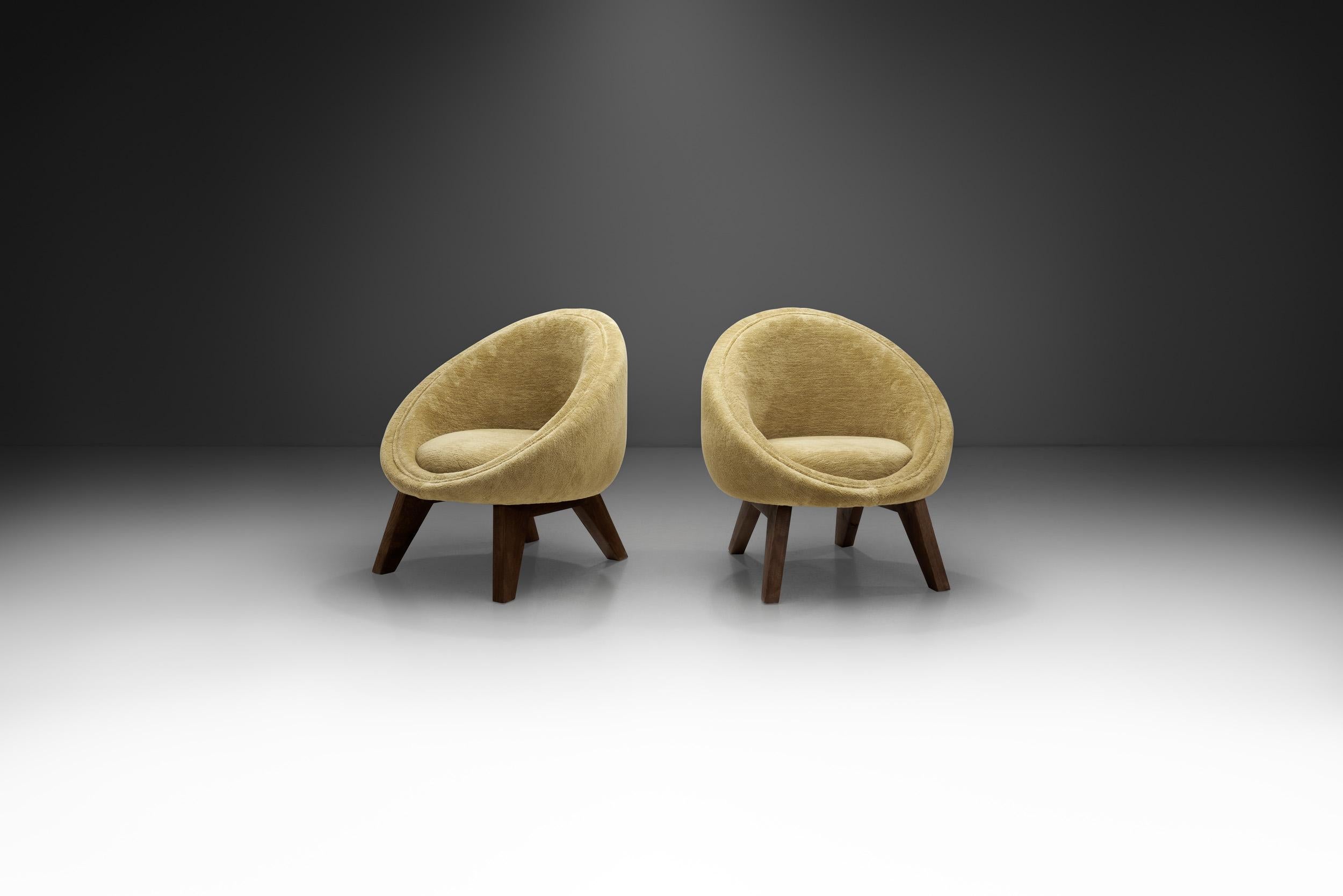 Cosy shapes and elegant hues come together to make this pair of easy chairs a stylish accent pieces that cannot go overlooked. Boasting strong curved lines, custom oak legs, and luxurious upholstery, the chairs’ tactile details add a soft artistic