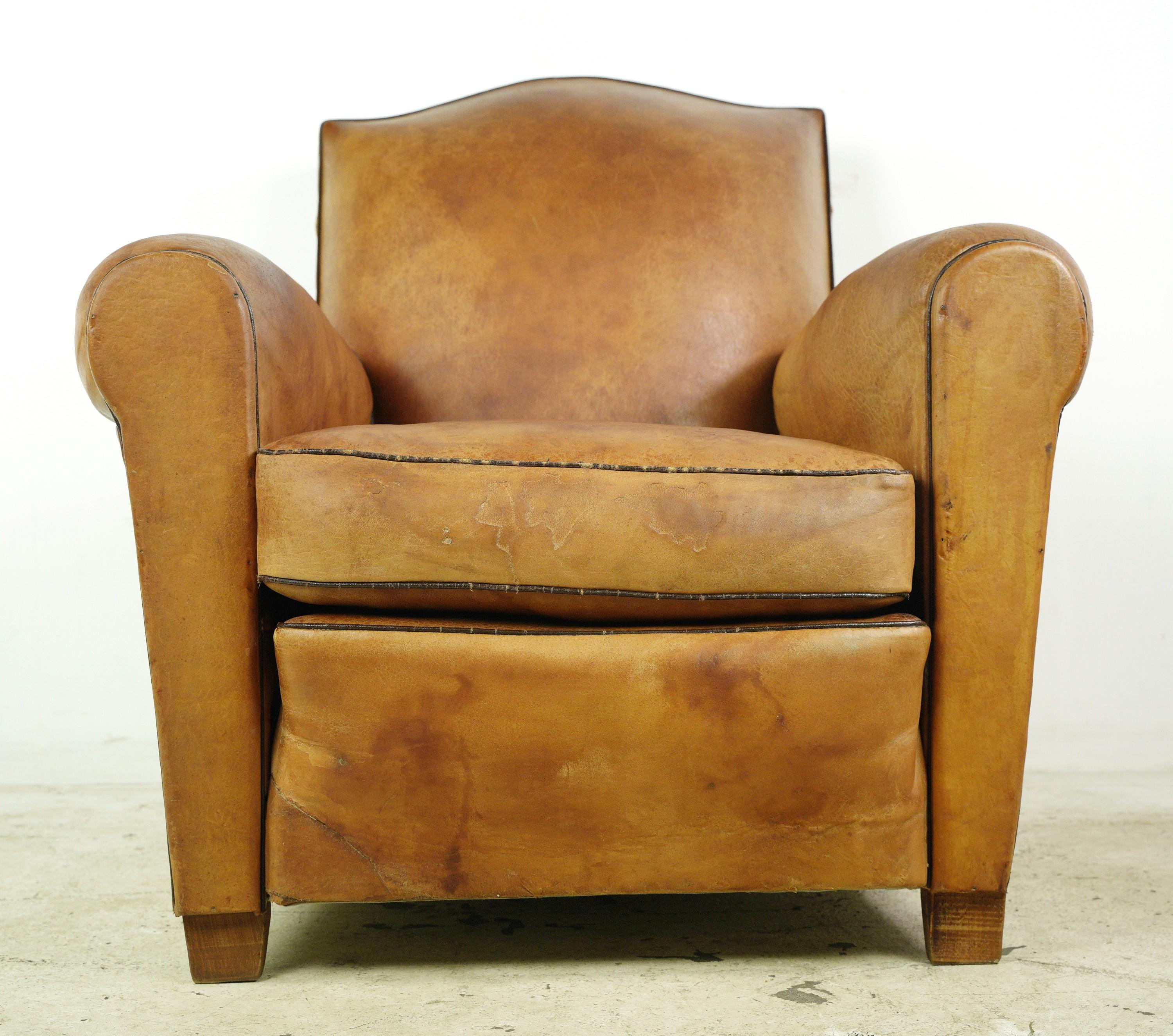 This European club chair is upholstered in tan leather, features a distinctive moustache shaped back and steel studs. This chair combines vintage charm with unique design elements, offering both comfort and visual appeal in a sophisticated seating