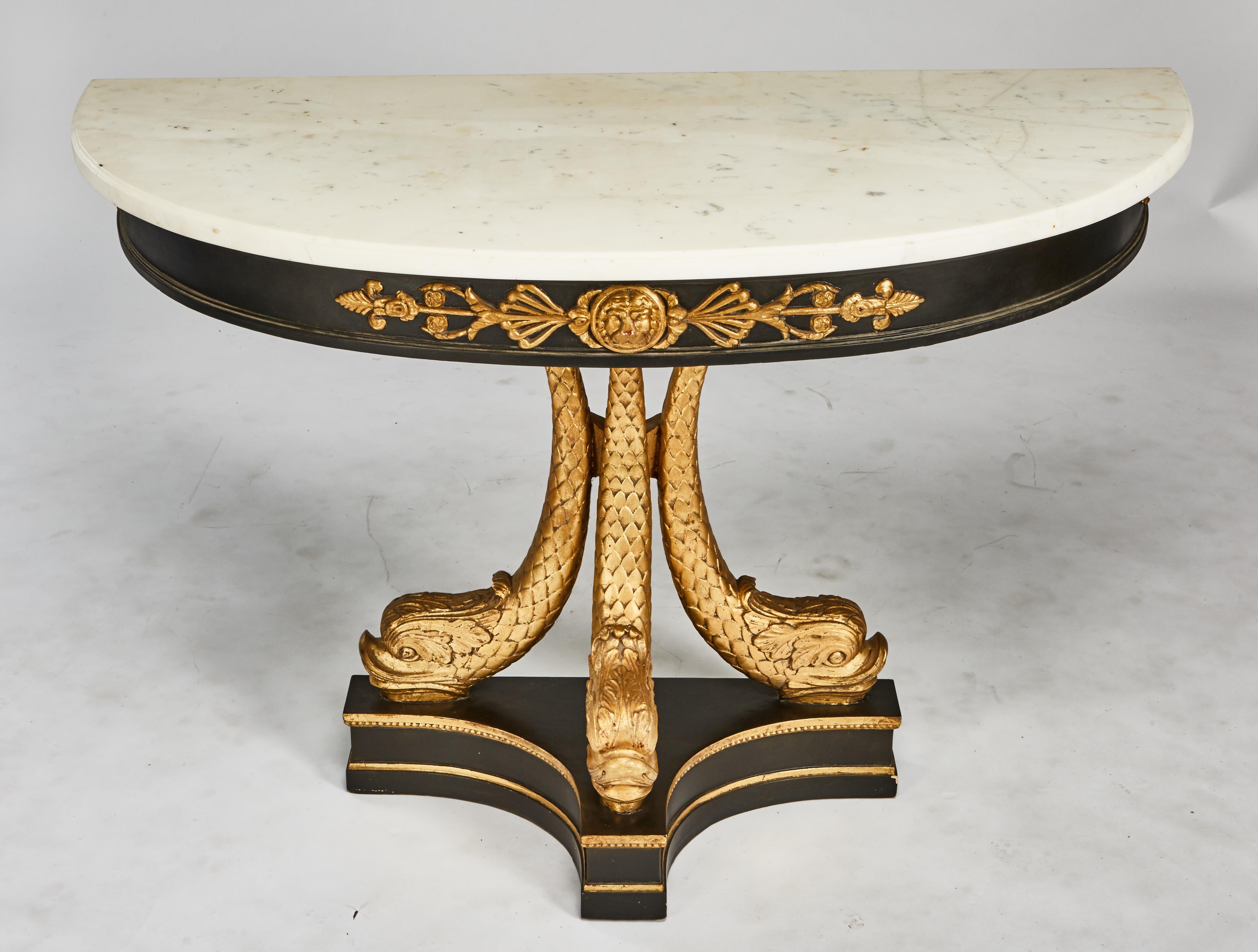 Early 19th century North European neoclassical ebonized & giltwood console with molded edged demilune white marble top, above a conformingly shaped frieze centering a lion mask raised on three dolphin supports on a convex plinth base. Older