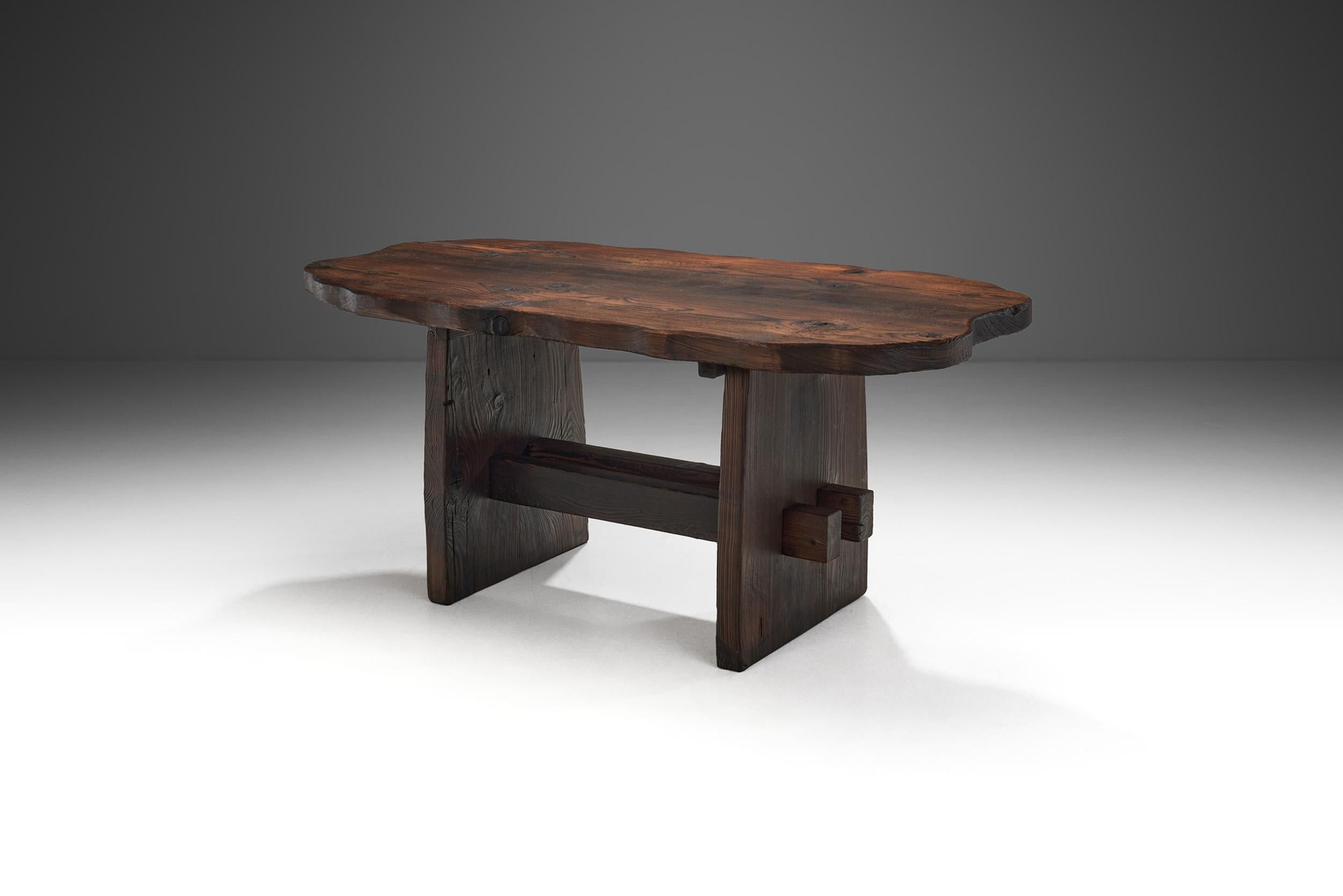With a robust organic form and an earth-toned palette, this dining table is the embodiment of 20th century brutalist design. It is somber, giving importance to eerie organic and rugged shapes in dark, earthy tones. The imperfections of the wood and