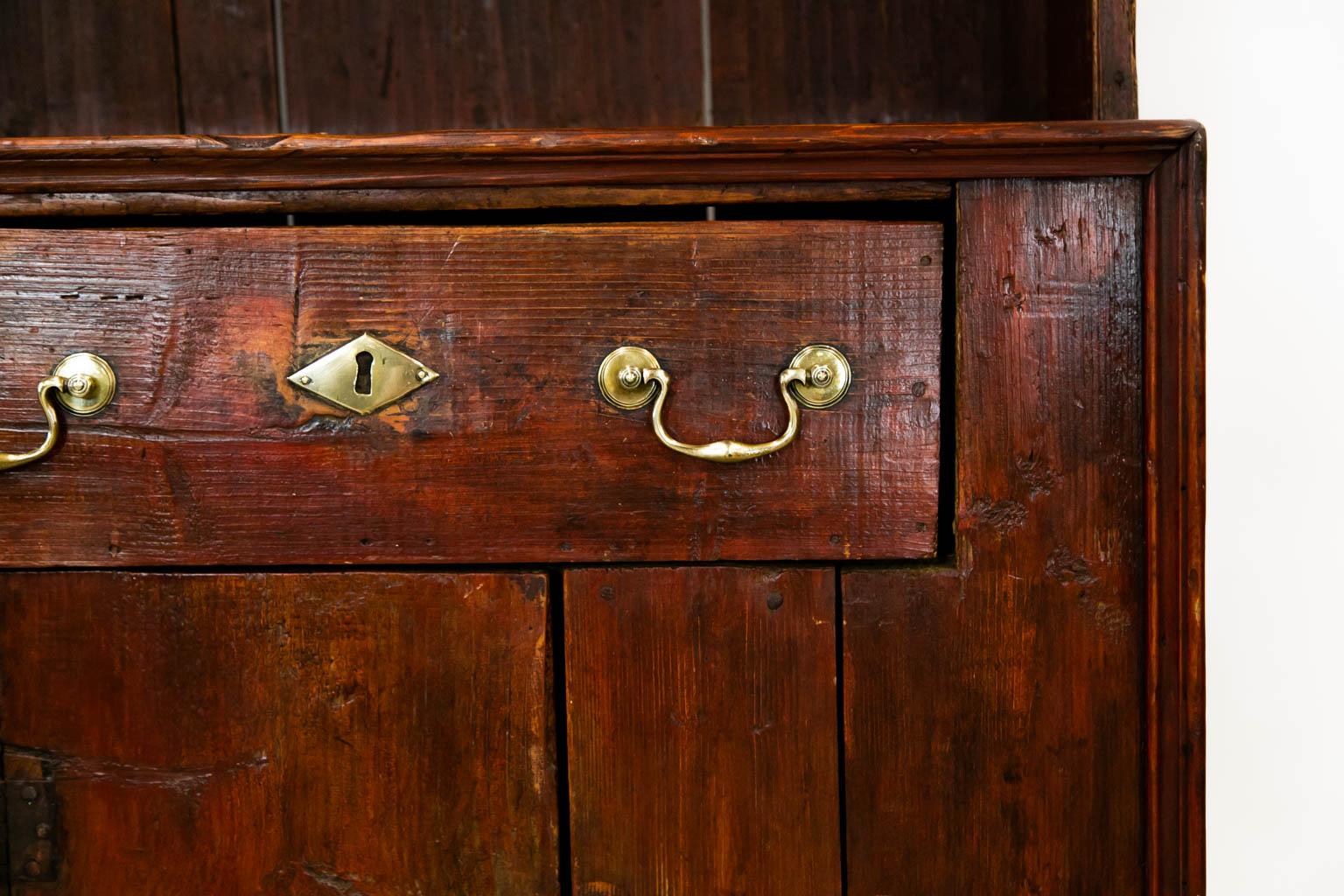 Questa credenza presenta resti della vernice rossa originale. La costruzione è a coda di rondine con mortasa e tenone. La parte superiore presenta un baldacchino sporgente con un grembiule sagomato e pendenti intagliati. La parte inferiore presenta