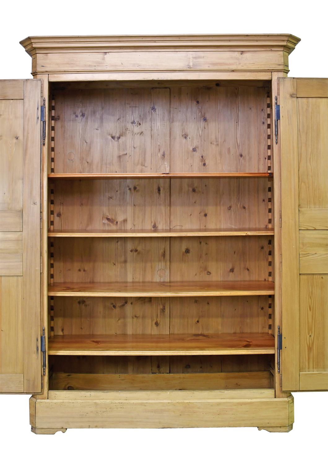 A charming wardrobe or armoire in a light honey-colored pine with two paneled doors & sides, and four adjustable interior shelves. Doors are on original steel butt hinges allowing them to open 180 degrees, with wooden key plate, original working