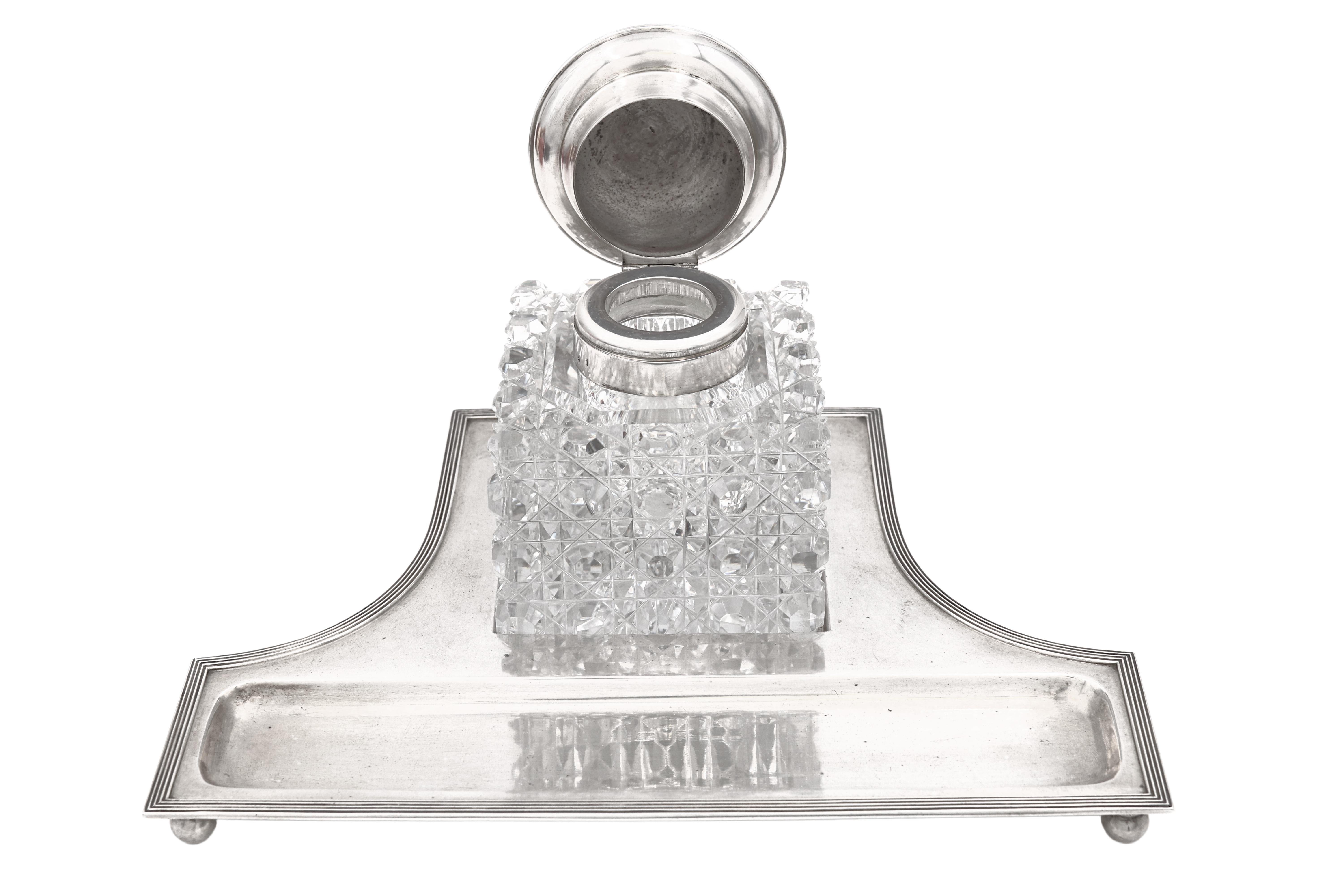 Central European silver and crystal glass inkwell on stand which has 4 balled feet and a rim with a geometrically-inspired pattern in Art Deco style. The stand measures 9 1/2'' in length by 6 7/8'' in width by 2/3'' in height and weighs 10.2 ozt.