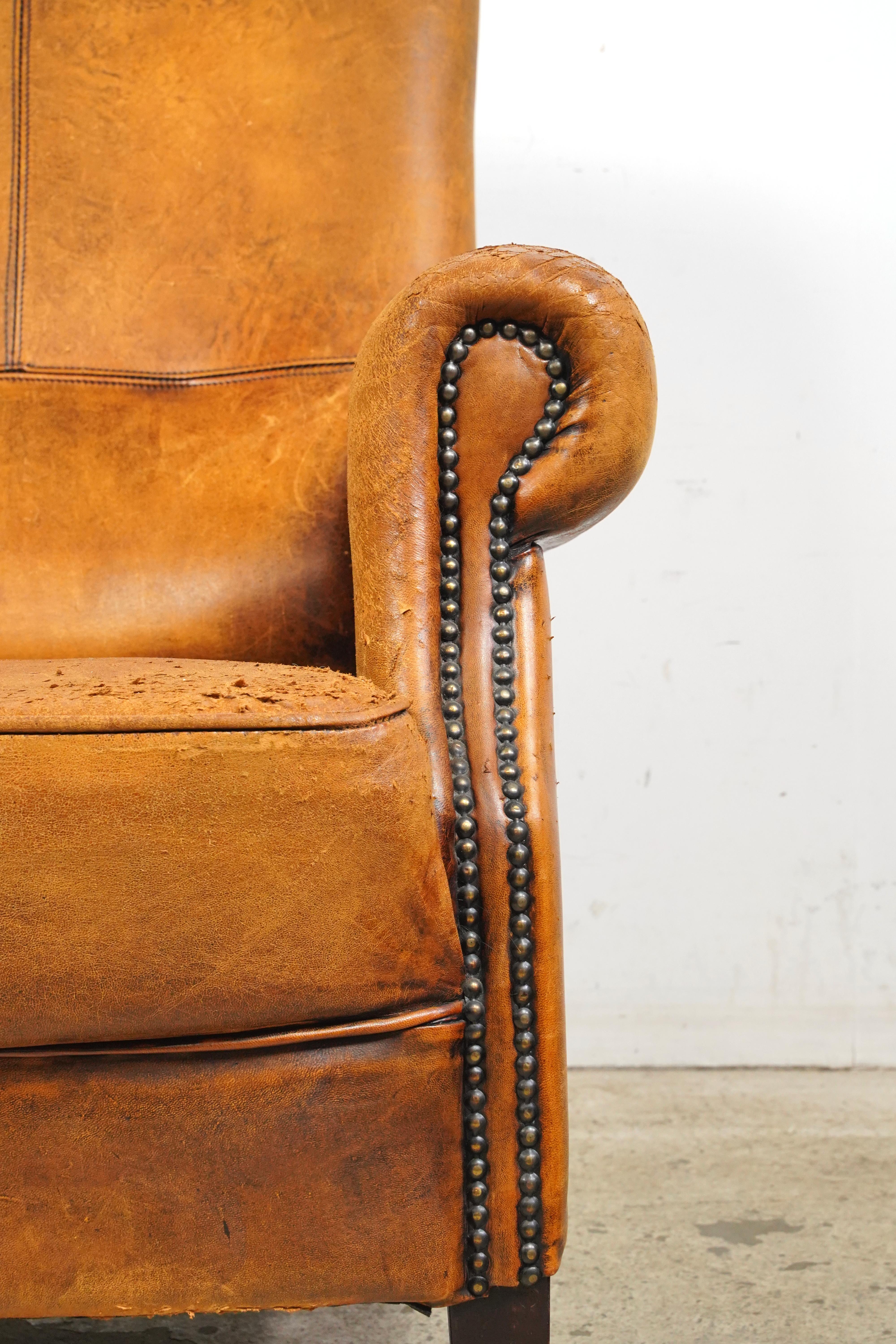 Fauteuil club en cuir marron clouté fabriqué en France. Il est orné de détails cloutés et de pieds en bois. Le cuir et les pieds présentent des signes d'usure et d'ancienneté. Veuillez vous référer aux photos pour une vue complète de l'état. Un