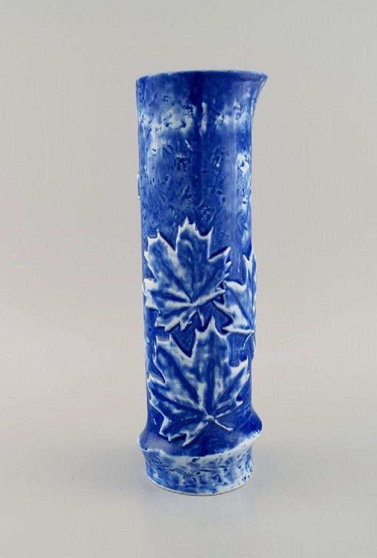 Céramiste d'atelier européen. Vase cylindrique en céramique émaillée, décoré de feuilles d'érable. 
Belle glaçure dans les tons de bleu. Fin du 20e siècle.
Mesures : 30 x 10 cm.
En parfait état.
Signé.