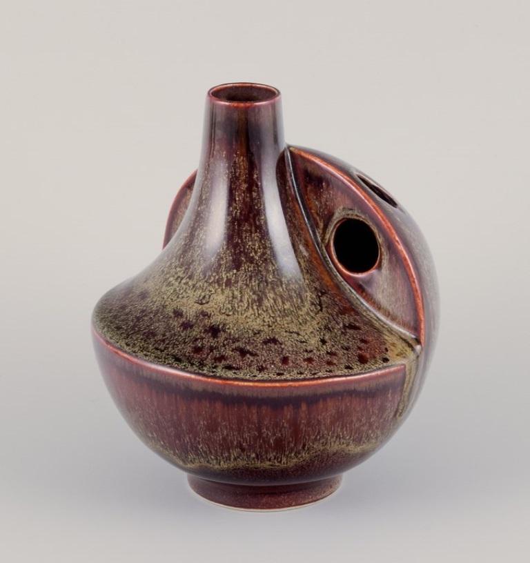 European studio ceramist. Unique ceramic vase with speckled glaze in brown tones.
Cubist shape with three holes.
1960s/1970s.
Perfect condition.
Indistinctly marked with a monogram.
Dimensions: Height 17.0 cm x Diameter 14.0 cm.
