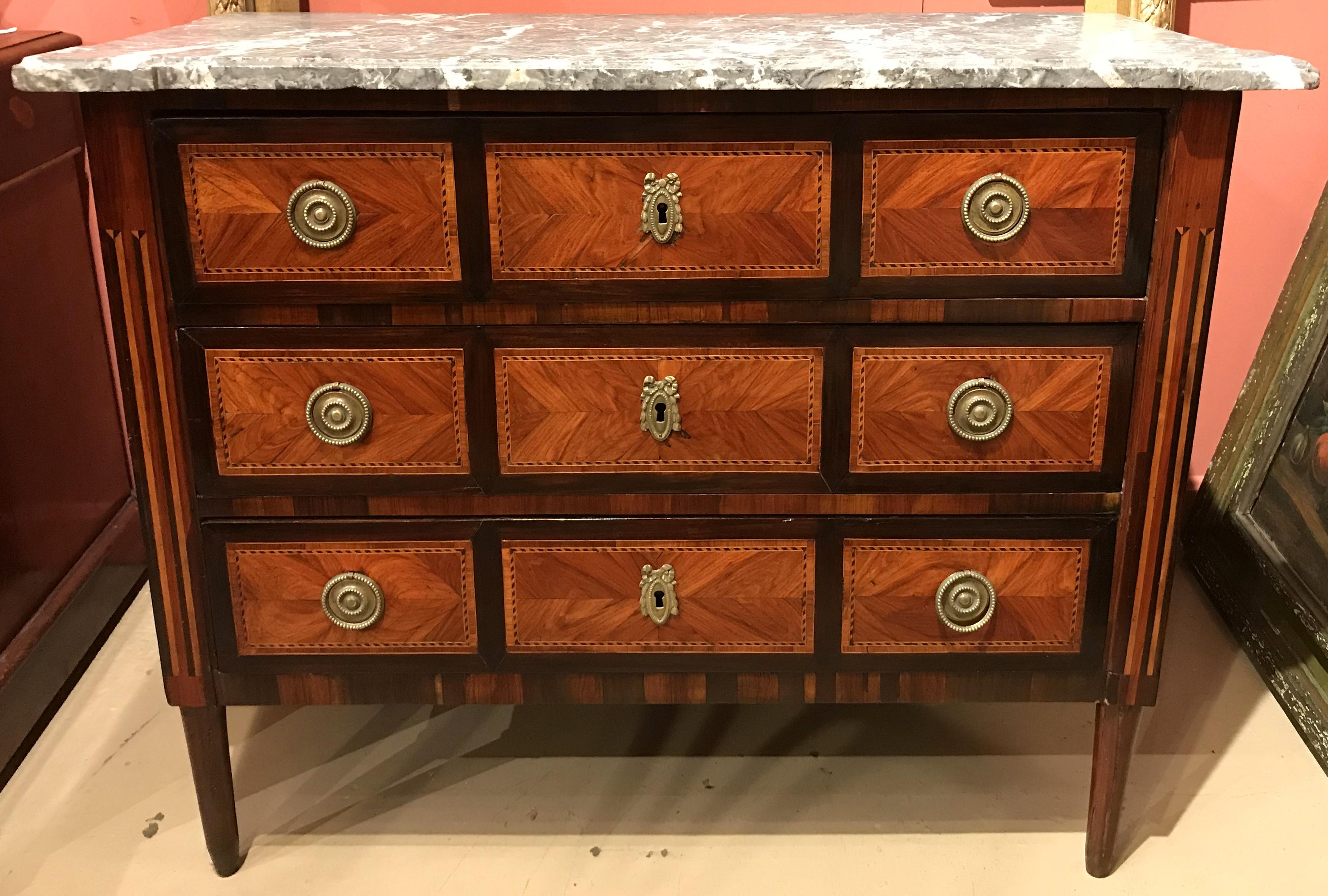 A beautiful mahogany chest of drawers with an associated gray variegated shaped marble top surmounting a case with three drawers, each with three bookmatched veneered cross-banded panels with checkered border accents and original brass ring pulls