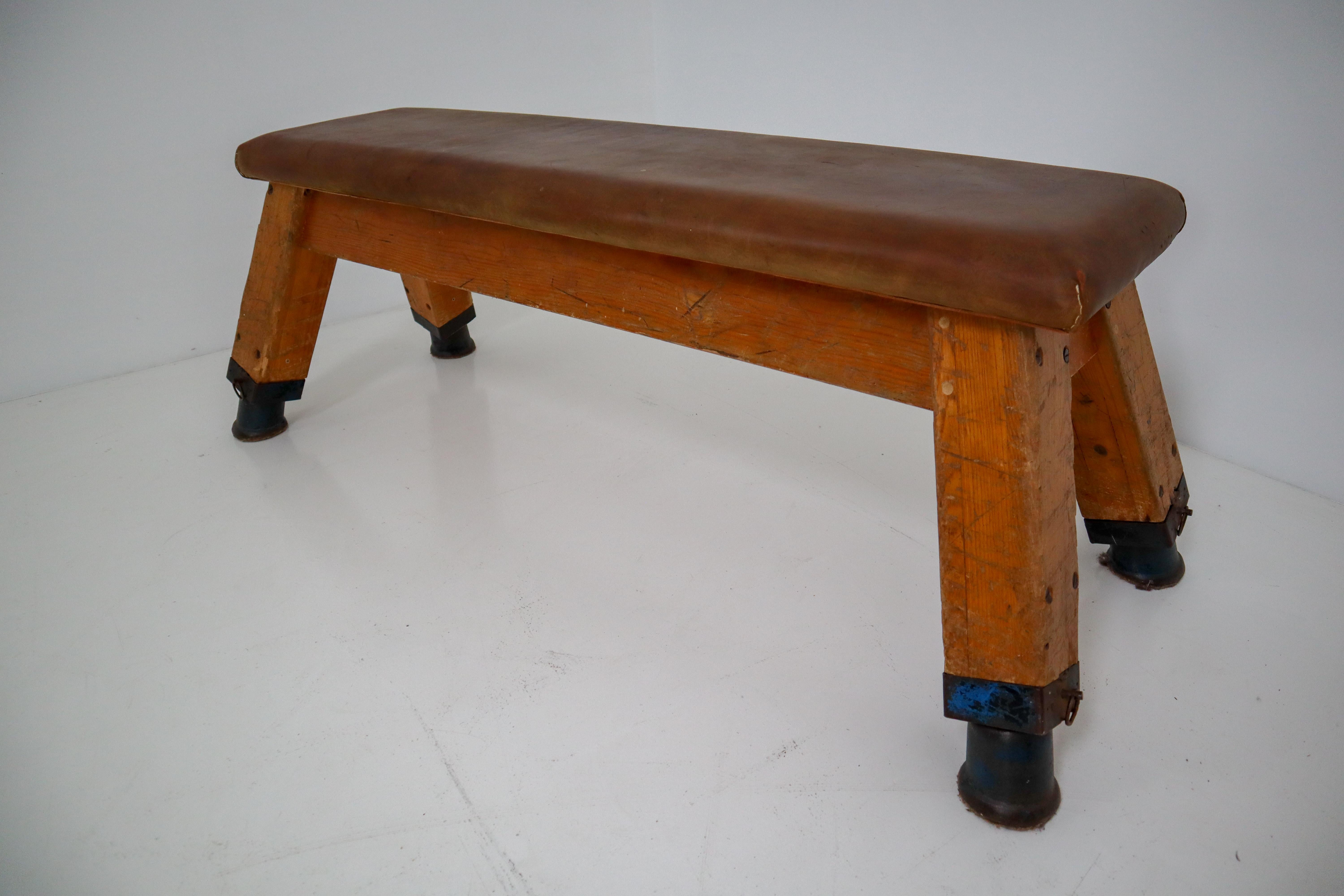 Strong, vintage European gymnasium bench with a patinated leather covered top that sits in to the bench's solid wooden frame. The gym bench frame maintains its original markings where the straps and rings were once held. Can be used as a coffee,