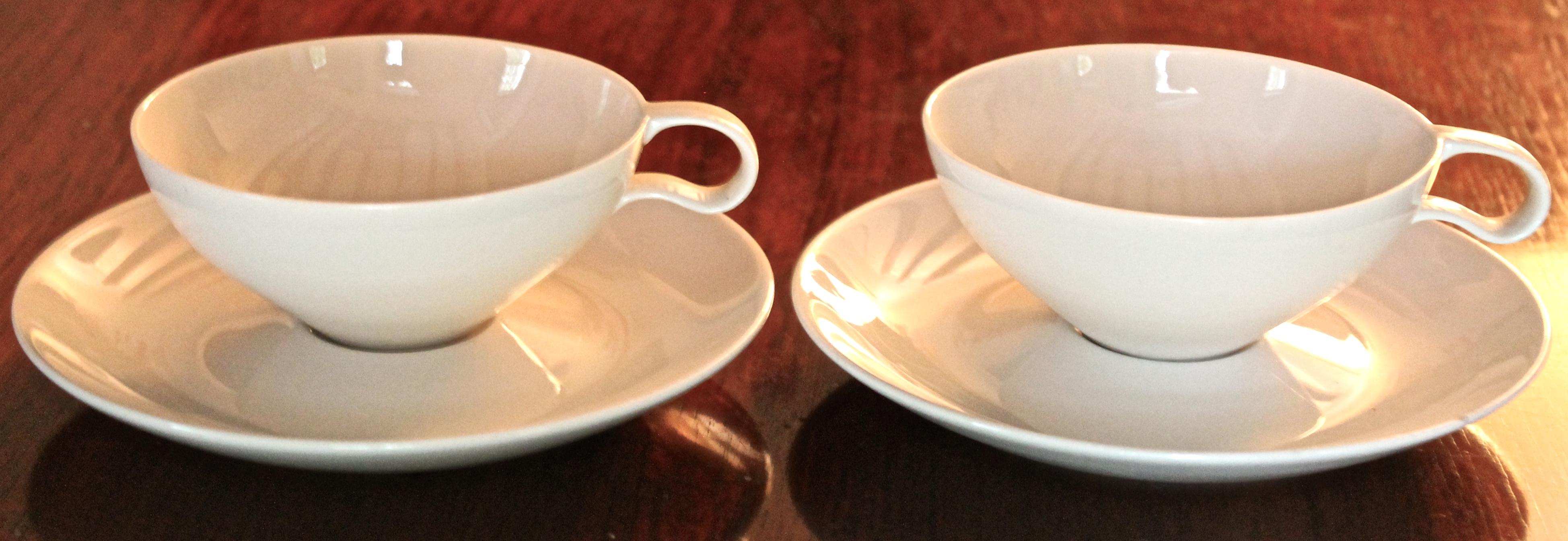 The original discontinued cups with the downward handles and golden tan added over the porcelain white from the famous set commissioned by The Museum of Modern Art (MOMA). Four cups and four saucers, most are signed. 