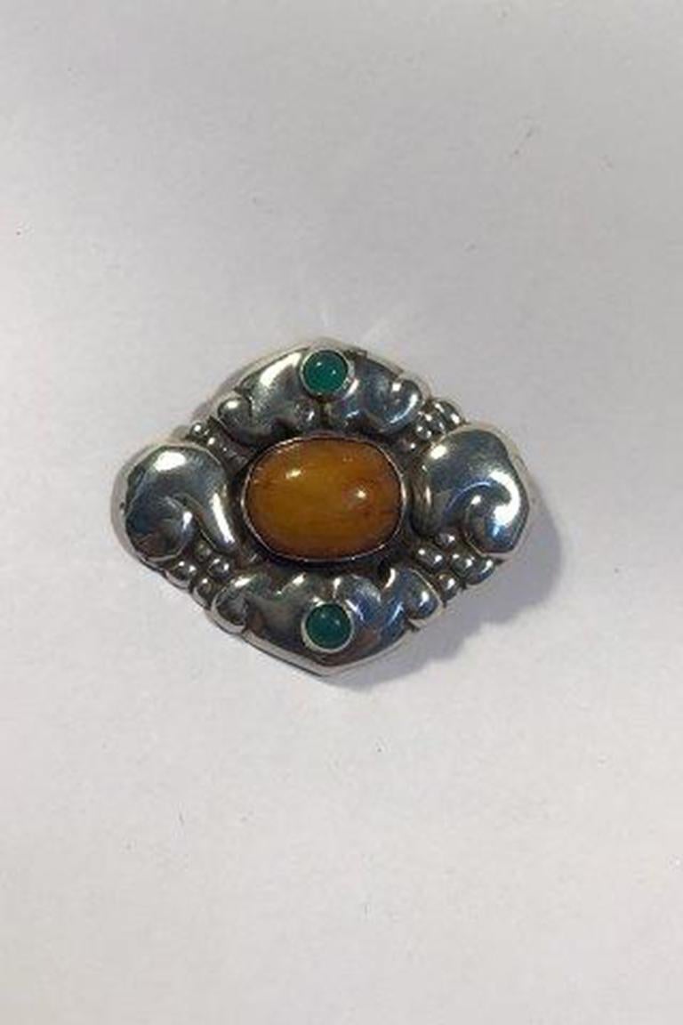 Broche en argent Evald Nielsen avec centre en ambre et pierres vertes Fermoir partiellement renouvelé.

Dimensions 5,6 cm x 4,6 cm/2.20