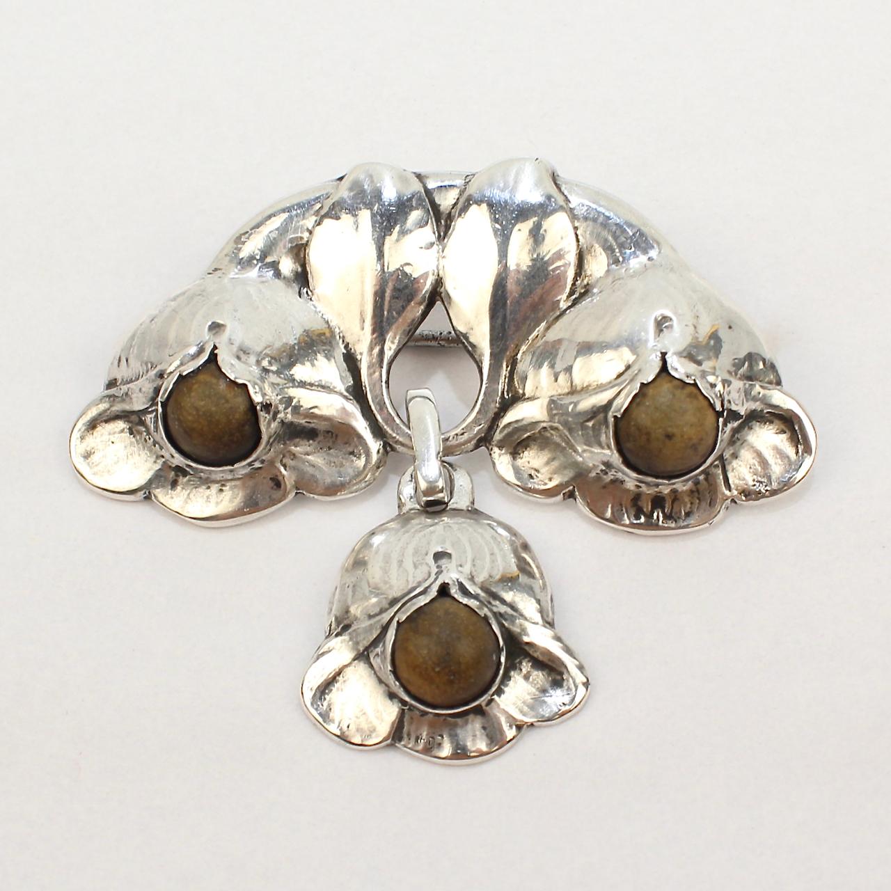 A very fine Evald Nielsen Skonevirke chandelier style brooch. 

The semi-circular top has two inverted flowers supporting an inverted floral pendant.

Each of the three flowers is set with a Jade (Nephrite) cabochon at its center. 

A wonderful