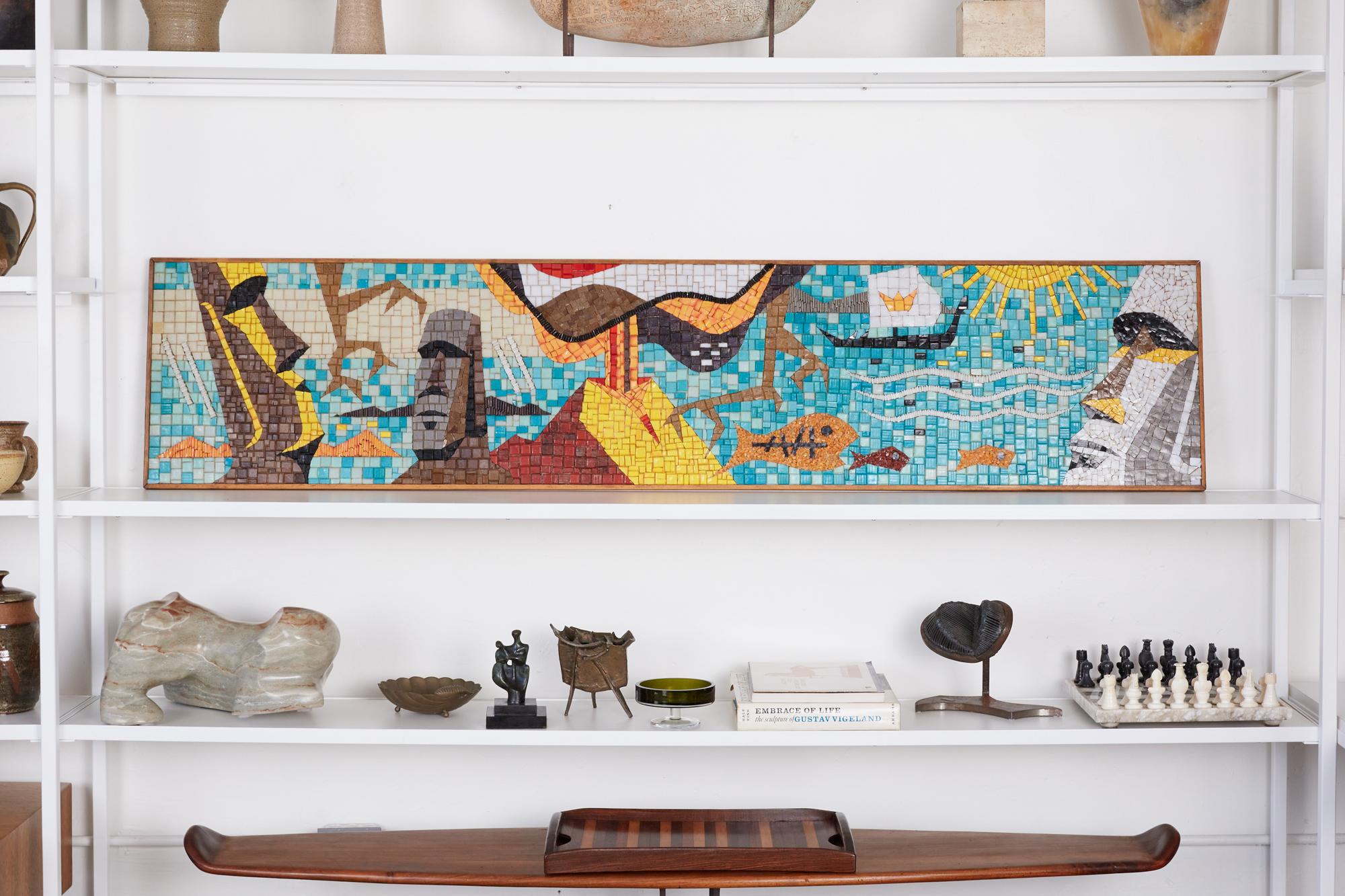 Mosaic tile wall art in the style of Evelyn Ackerman, circa 1970s. The wall art piece features a depiction of a volcanic mountain, fish in the ocean, and the carved stone figures, or Moai on Easter Island in Polynesia. The scene is made of multiple
