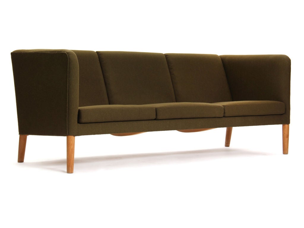 The even arm sofa by Hans Wegner, manufactured by master cabinetmaker AP Stolen. A high, even arm three seat sofa on tapered oak legs upholstered in olive green wool.