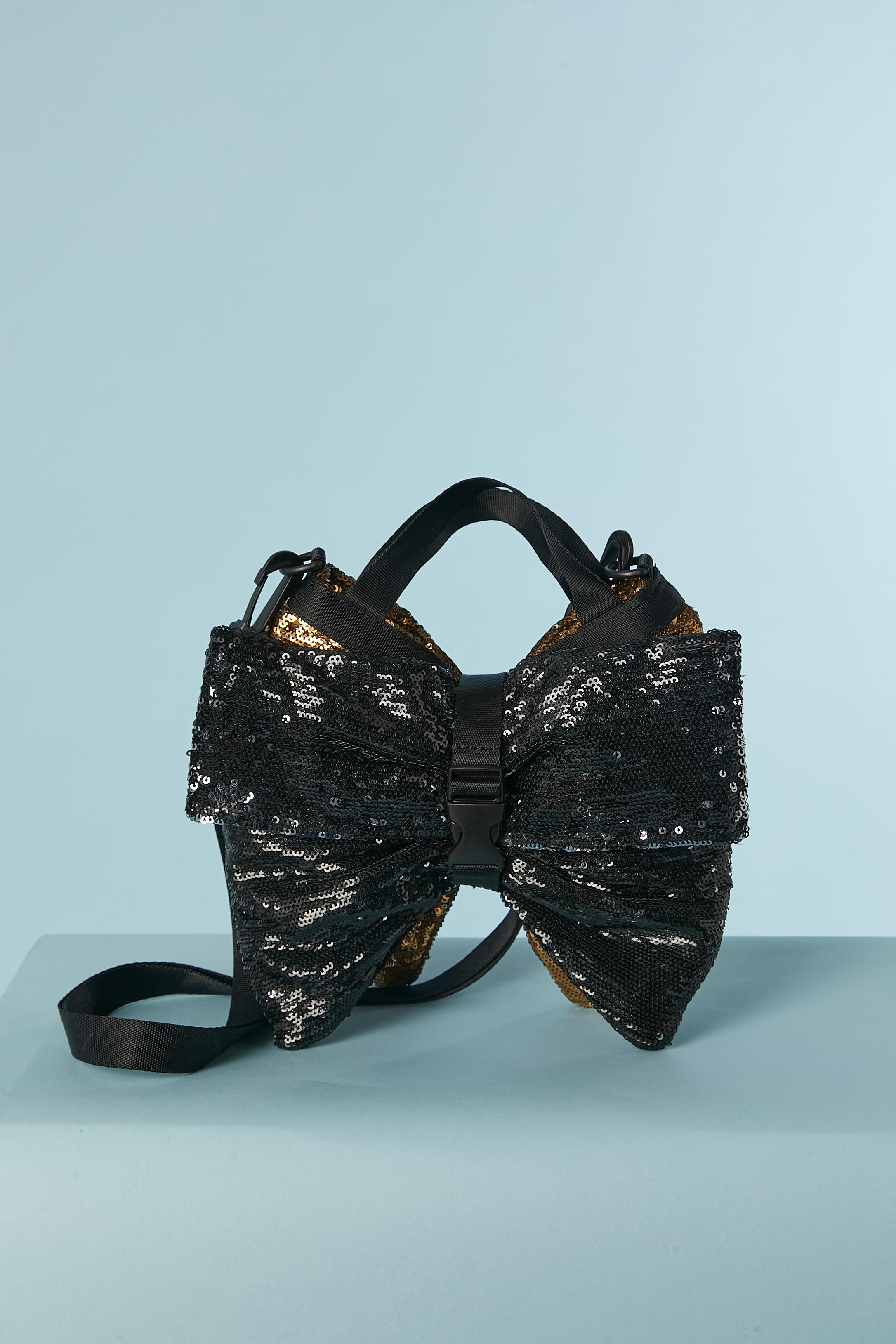 Evening bag in black and gold sequin with technical straps. The bag is made of 2 compartments, the gold one has a zip closure and the black compartment has a magnetic closure with a flat pocket inside. 
Black nylon technical hand straps and
