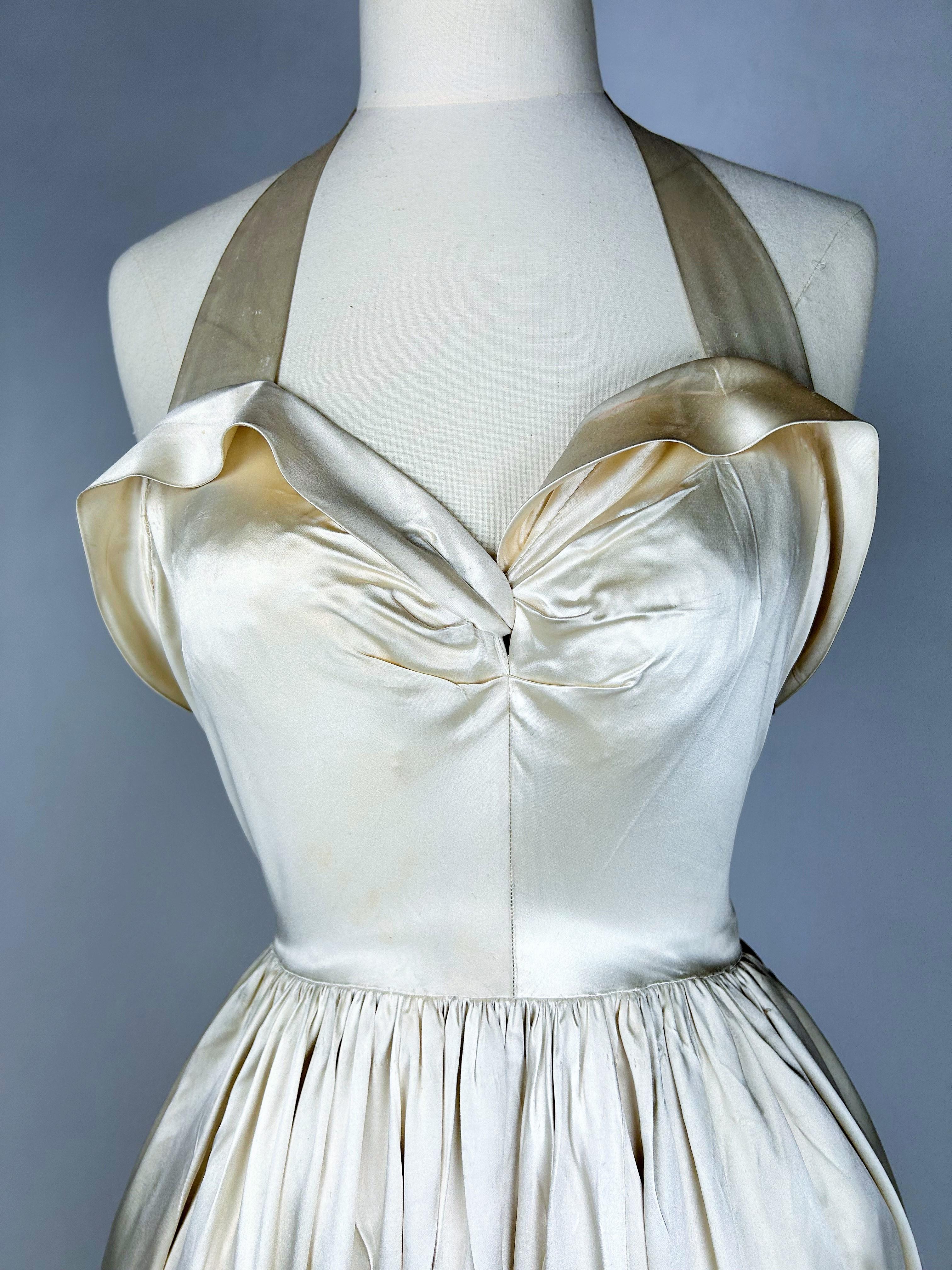 Circa 1940-1944

France haute Couture

Majestic grand soir dress in Duchesse Champagne satin by Lucien Lelong, 16 Avenue Matignon Paris and numbered 53368. Dress with large balconned neckline, held in place by a neck loop, side zipper.  Sun skirt