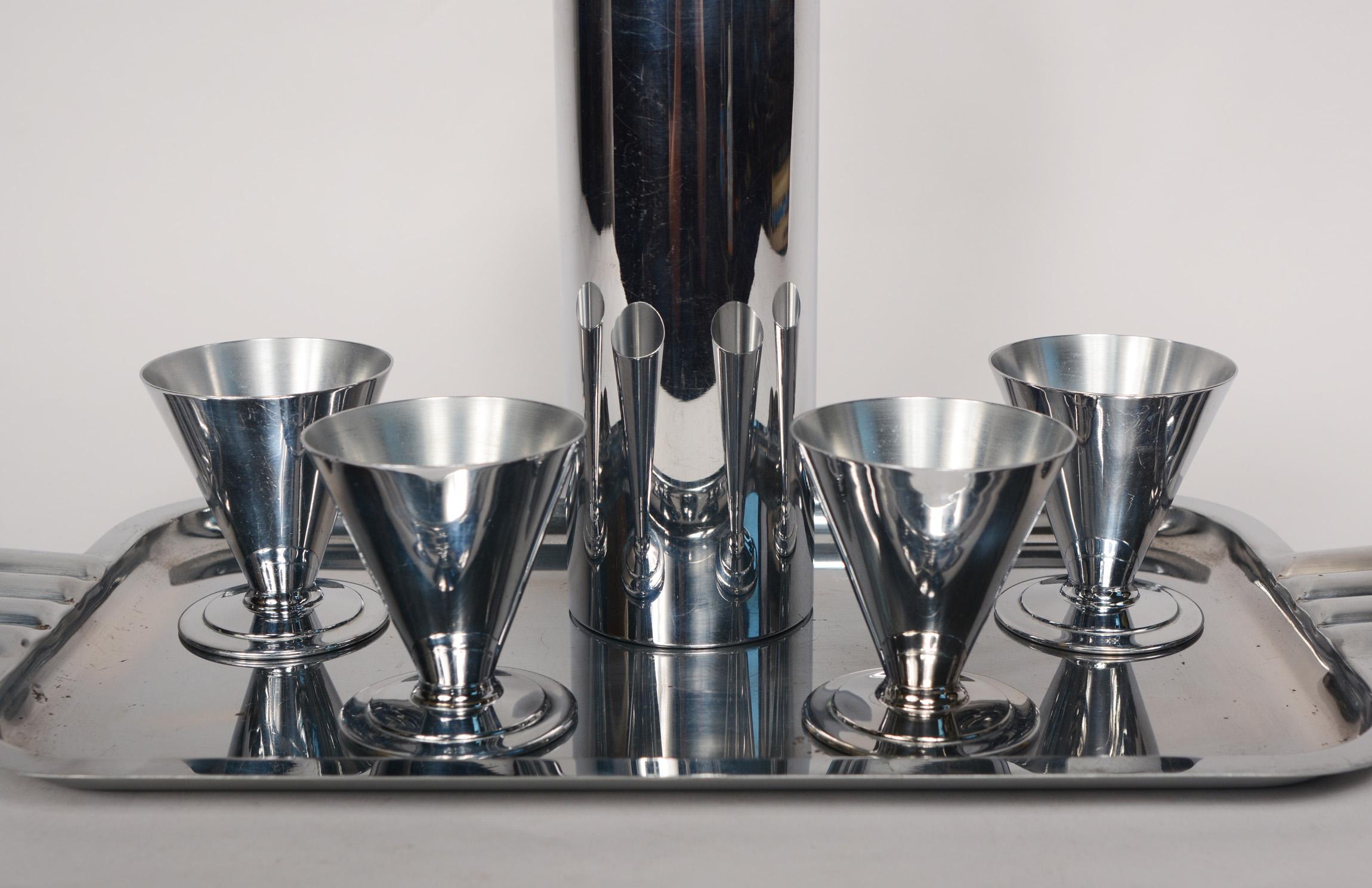 Machine age chrome cocktail set made by Evercraft. This set consists of a shaker, four cups and a tray. The cups are a scarcer design by Evercraft. The shaker has a built in strainer. The shaker likely originally had black paint in the recessed