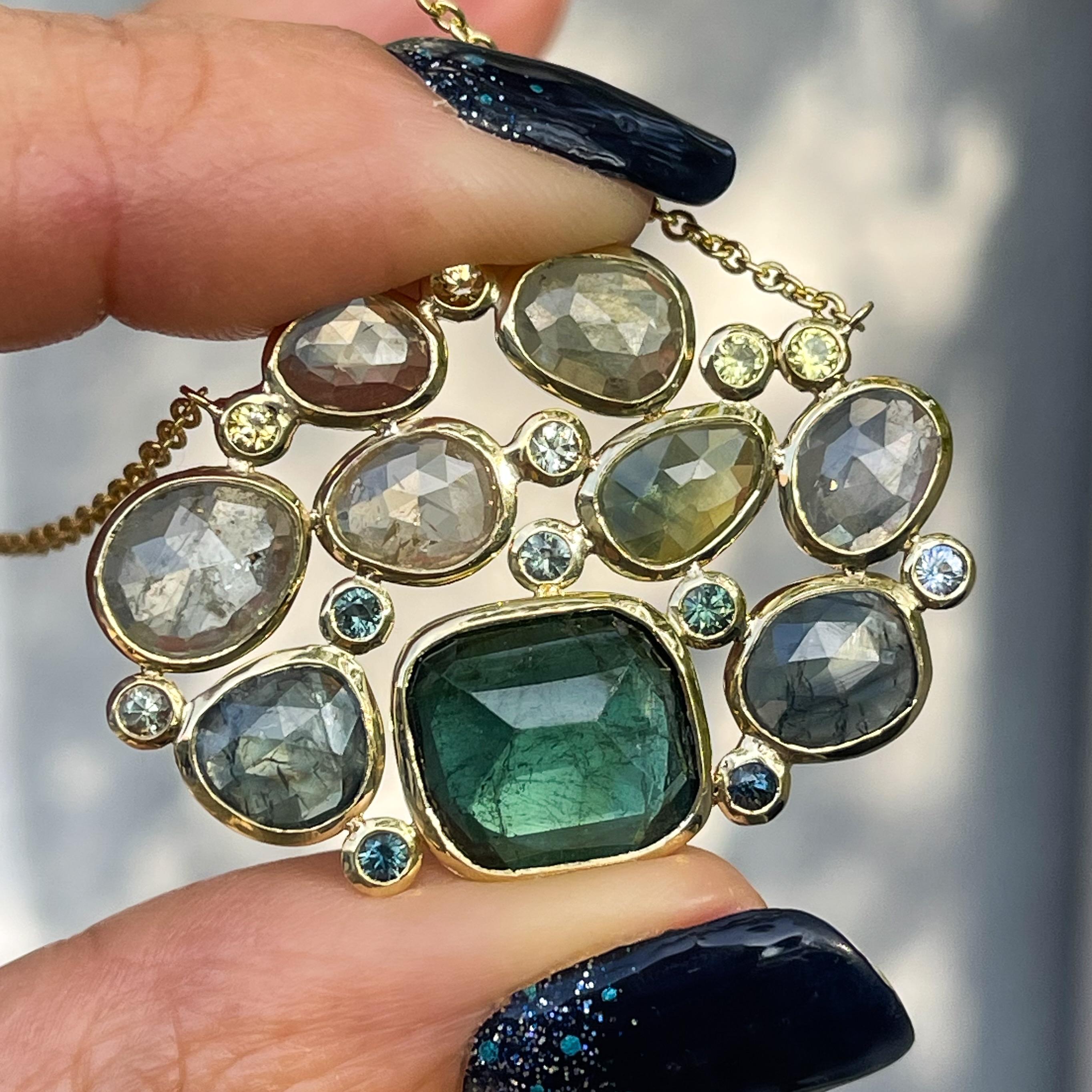 A deep teal tourmaline meets a tapestry of green sapphires in this tourmaline and sapphire necklace. Both the brilliant cut and rose cut gems draw upon nature's earthy tones, sapping its hues as though extracted directly from the forest. A