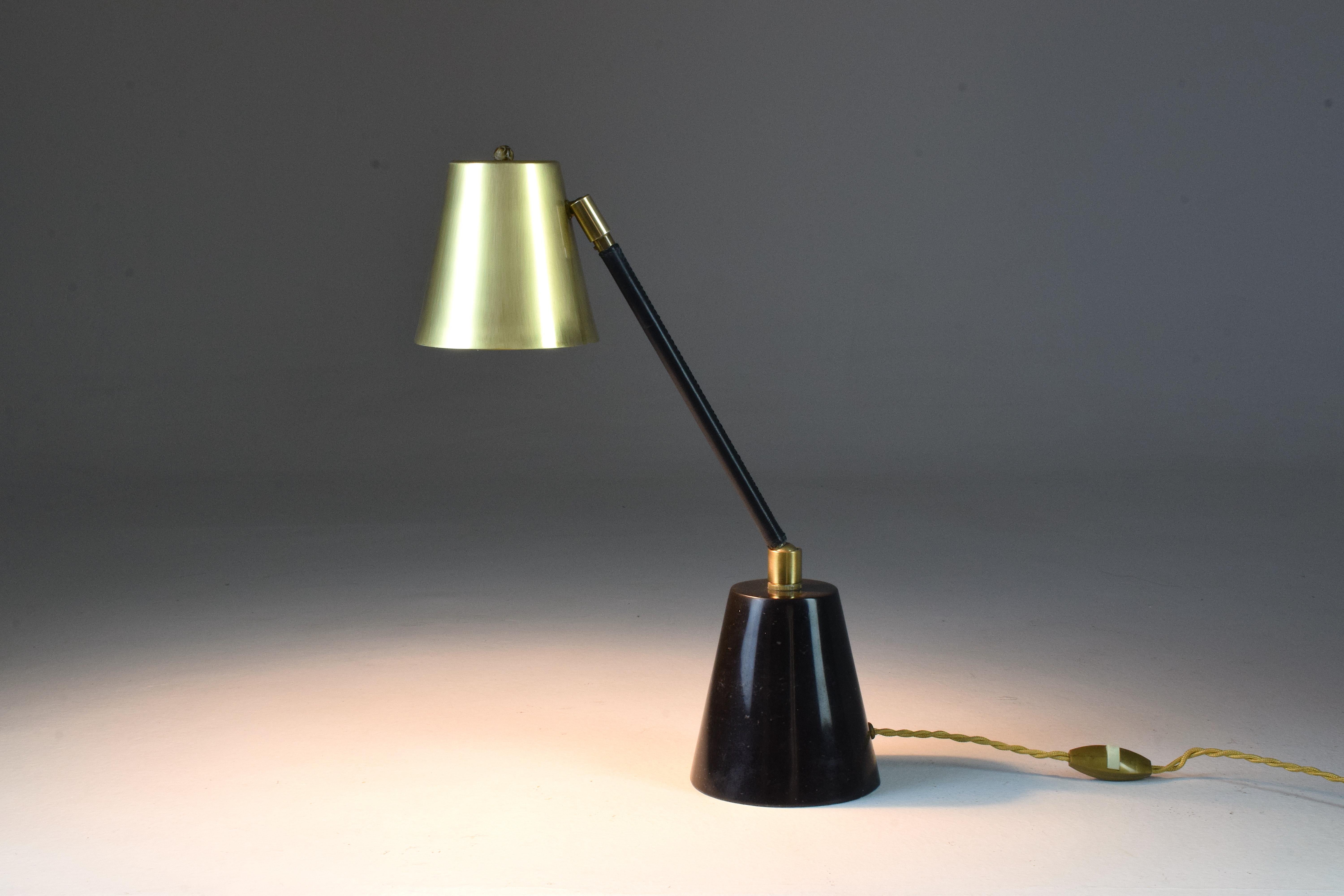 Contemporary handcrafted articulating table lamp designed in a gold polished brass stem adorned with a black sheathed leather detail hand sewn by artisan saddle makers which articulates at the base with a ball joint. The shade is designed out of