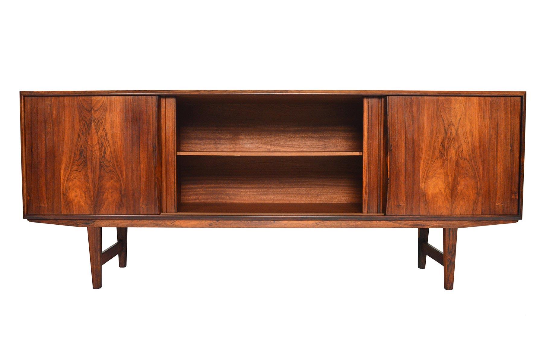 Beautifully simple and effortlessly modern, this Danish modern credenza in rosewood was designed by E.W. Bach for Sejling Furniture Company in the 1960s. Four sliding doors with grooved pulls open to reveal three bays with adjustable shelving. The