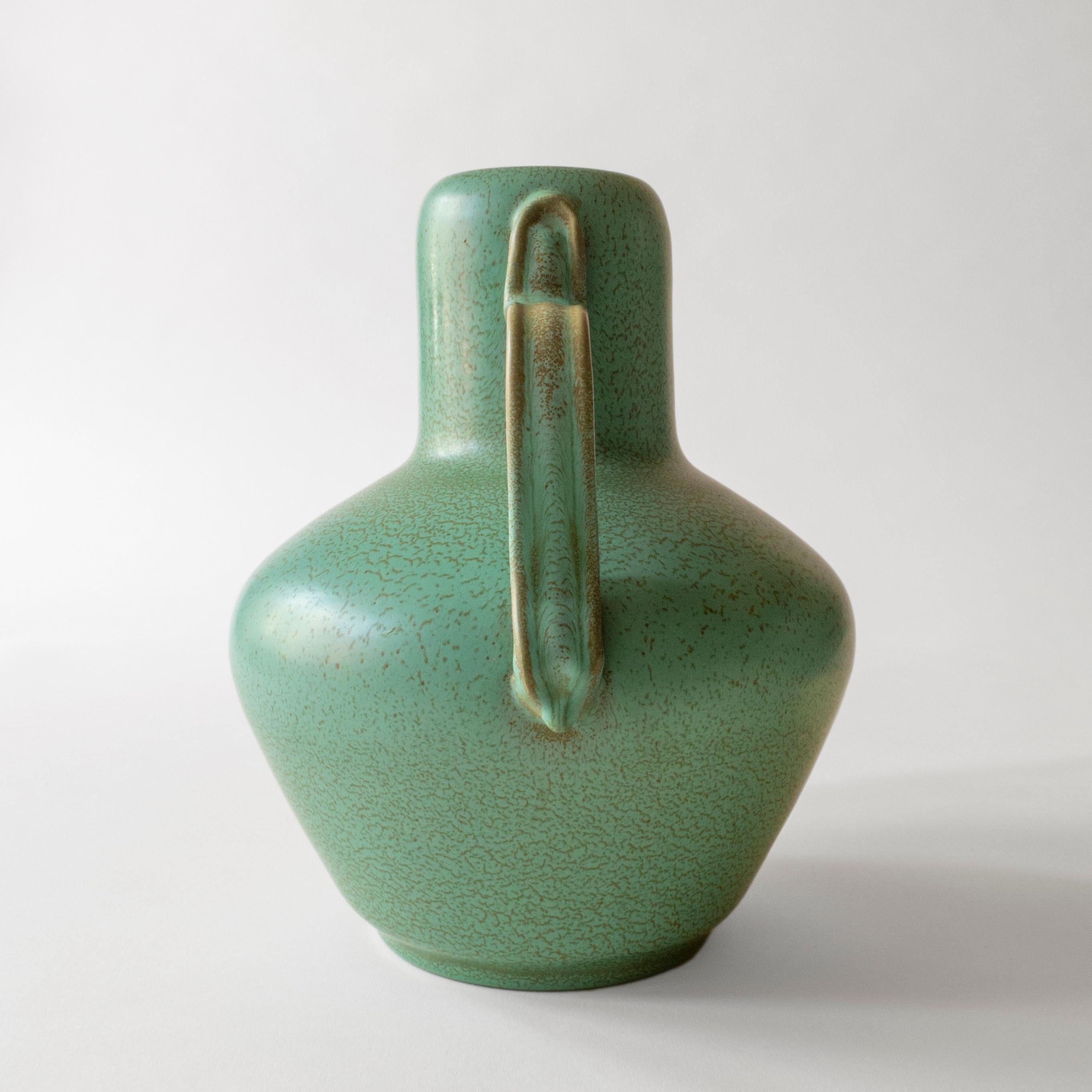 Each shaped handle, elegantly applied to the pared-down, modernist vase, speckled drip glaze in green and emerald hues throughout. Marked underneath: D183 SMARGAD (Emerald) Bo Fajans

Ewald Dahlskog (1894-1950) was an renowned Swedish artist of