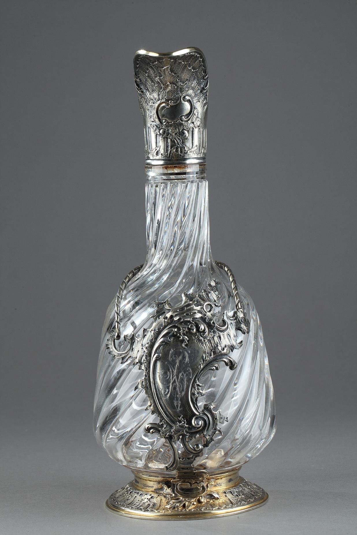 Ewer in crystal and cut with gadroons. The crystal is set in a silver setting with a rococo cartel decoration shredded on the body. The handle is divided into two parts and the neck is finely chiseled with patterns of grooves and rocaille. The grip
