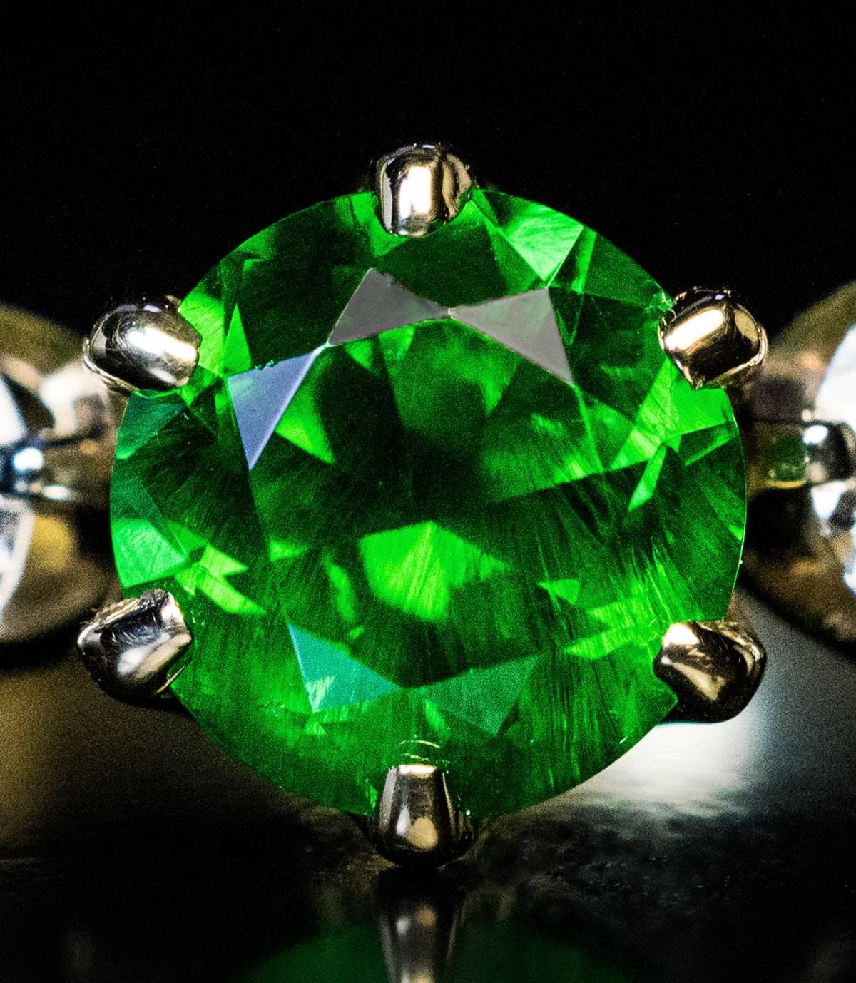This 18K gold contemporary ring features a top quality 1.67 ct brilliant cut Russian demantoid garnet flanked by two bright white round diamonds (0.54 ct total weight, F color, SI1 clarity). The demantoid has two beautiful “horsetails”.

Russian