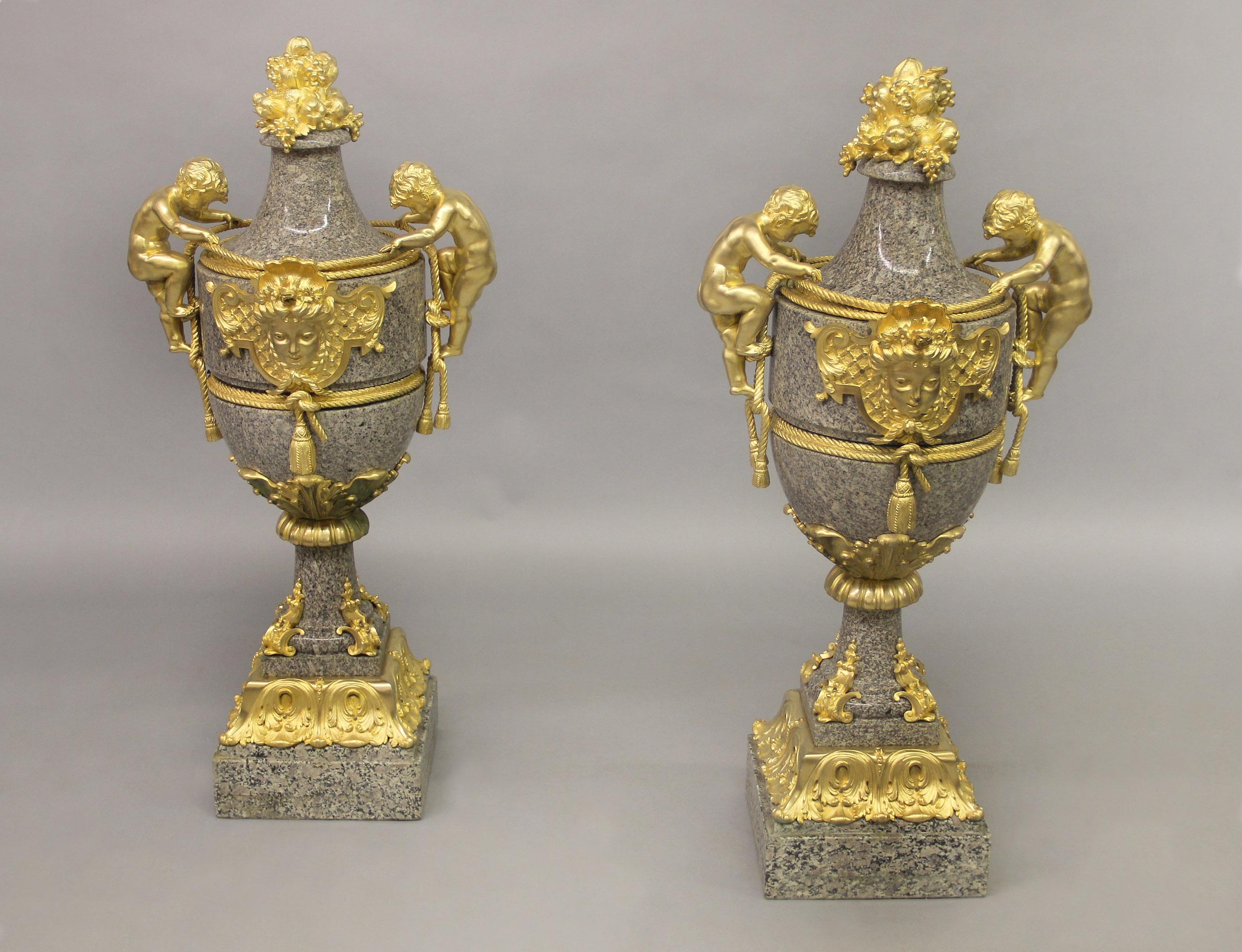 An excellent quality pair of large late 19th century gilt bronze mounted granite vases

Each vase surrounded by bronze rope and tassels with large climbing putto handles, centered with a beautiful female mask, the top with fruiting finials and the