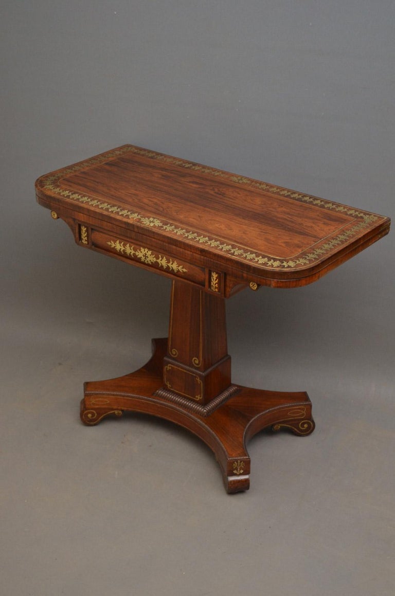 Sn3581, exceptional Regency, brass inlaid rosewood card table or games table with stunning brass inlaid fold over top enclosing baize lined games surface above brass inlaid frieze, raised on elegant column with quadrant beading to edge, terminating
