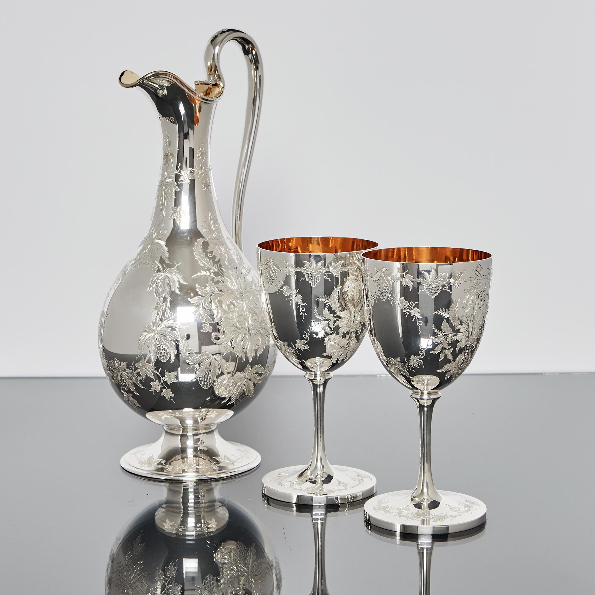 Pair of Victorian silver wine goblets and matching silver wine jug, housed in their original blue velvet-lined oak case. This beautiful and elegant set is hand engraved in fine detail with foliage, grapes and vines while the interiors of the jug and